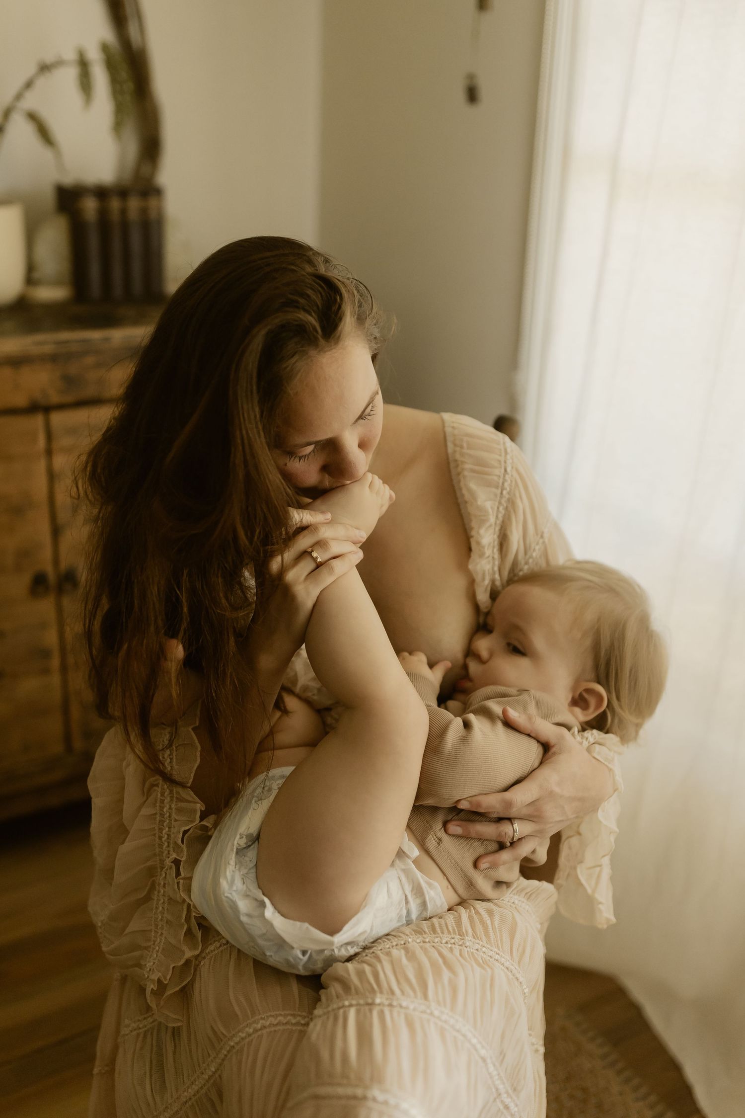 Candid family photography capturing gentle embrace in bedroom with soft window lighting.