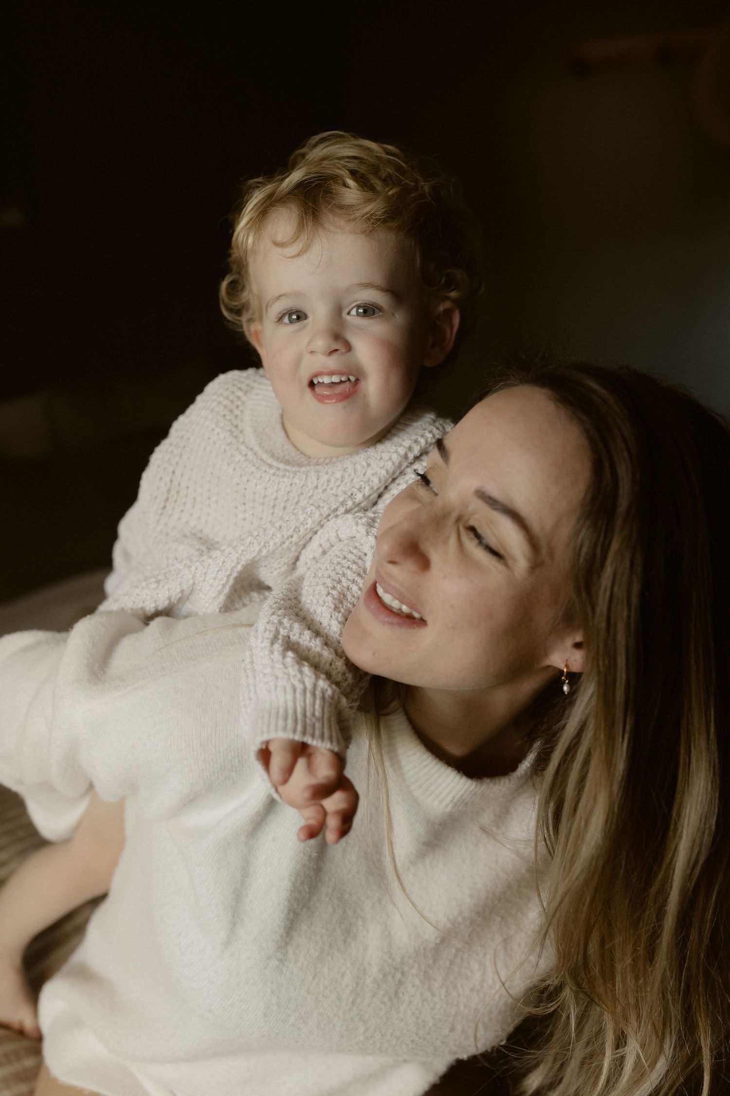 Joyful indoor portrait showing warmth and laughter in matching cream sweaters.