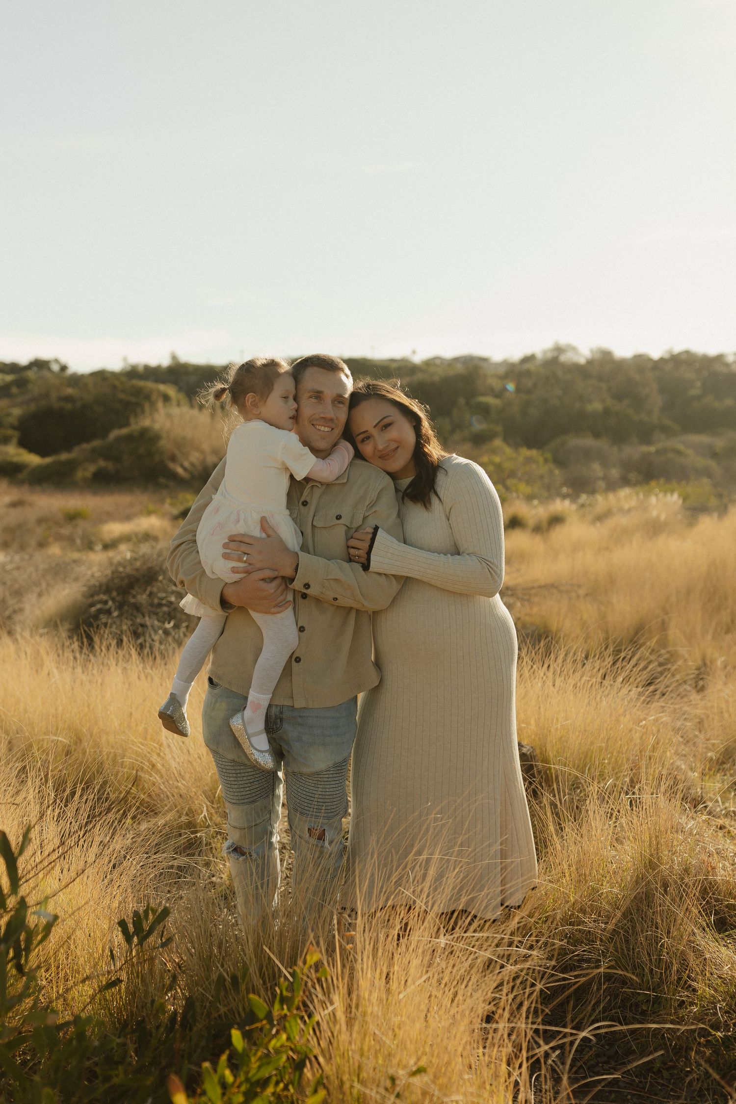 A tender family moment captured in warm sunlight amidst tall golden grass.