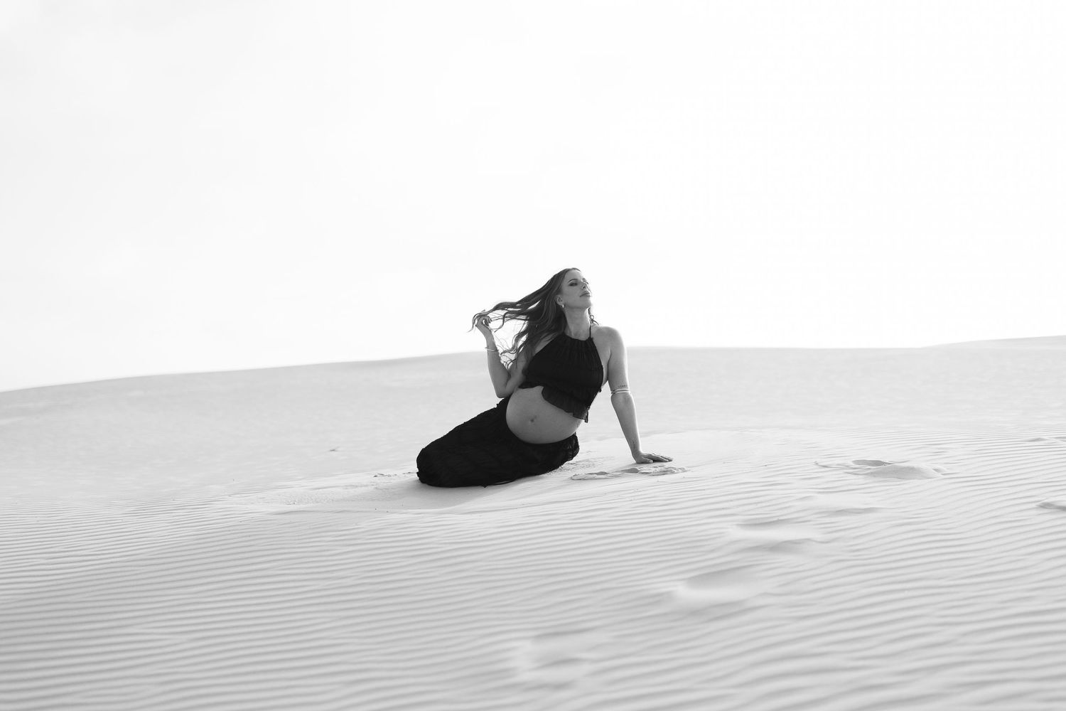 Artistic black and white photo of person reclining on sand dunes in desert landscape.
