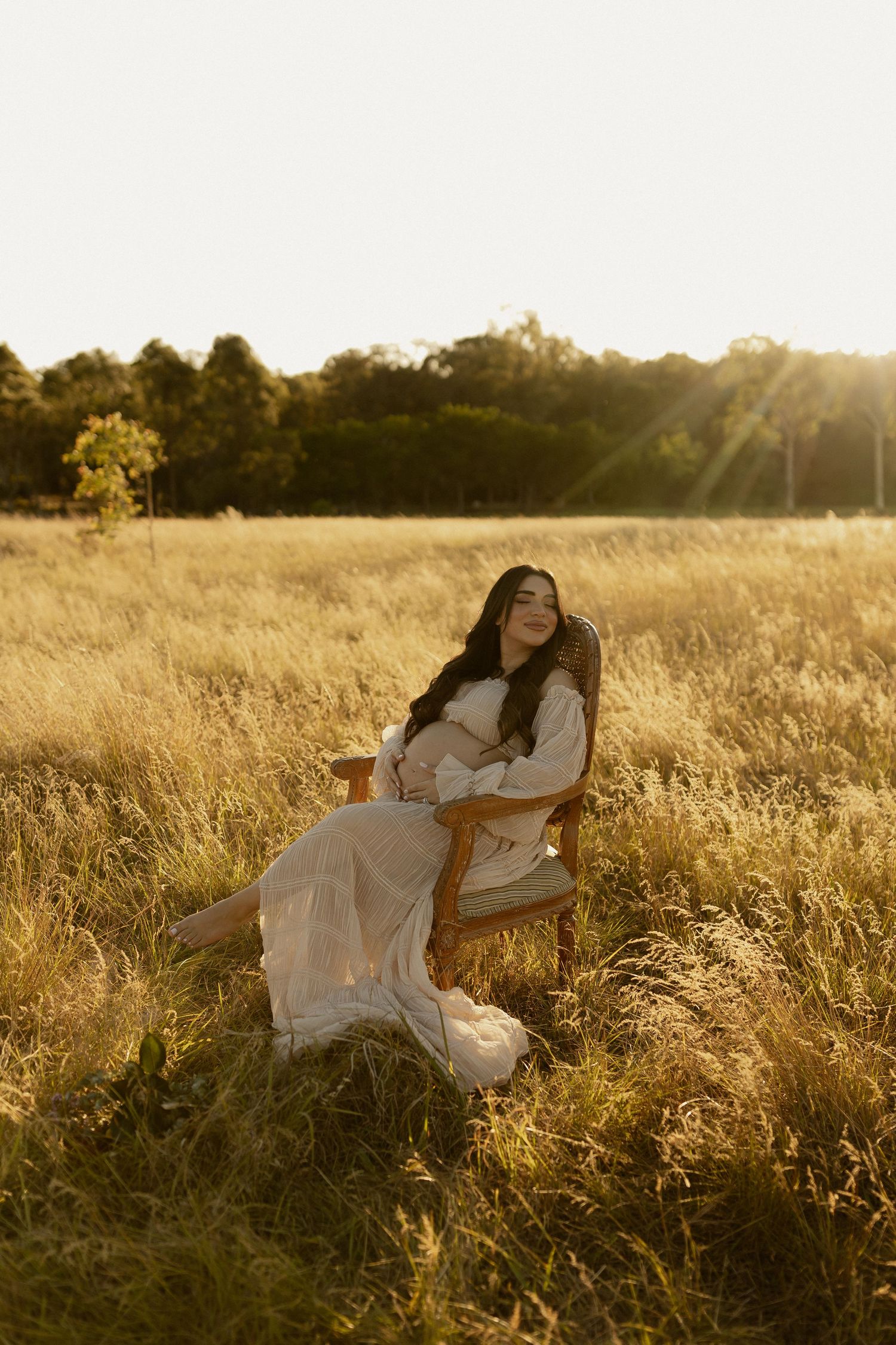 Person in white dress reclining in tall grass meadow at golden hour.