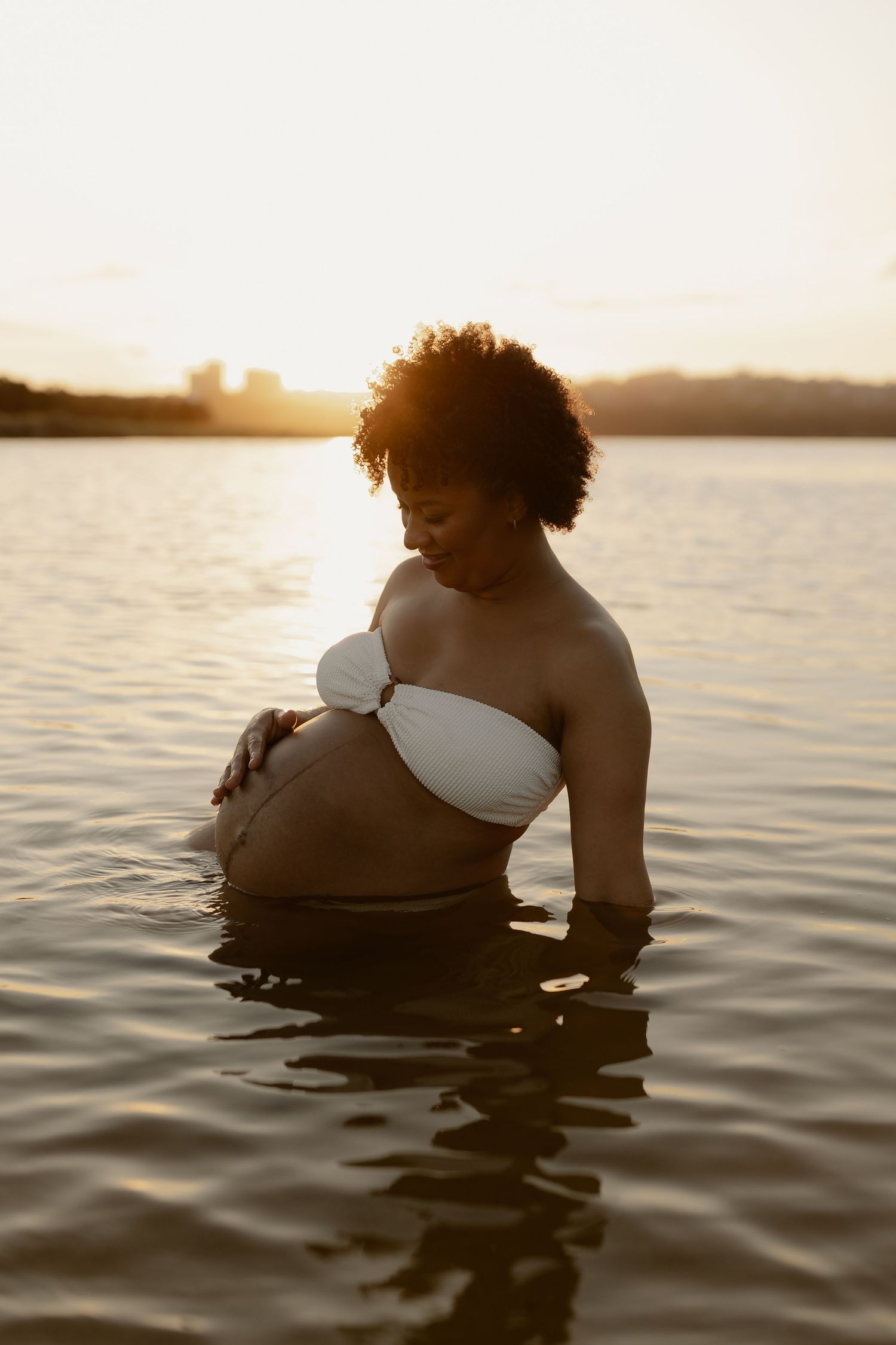 A silhouetted figure in white floats peacefully in calm waters during a serene sunset.