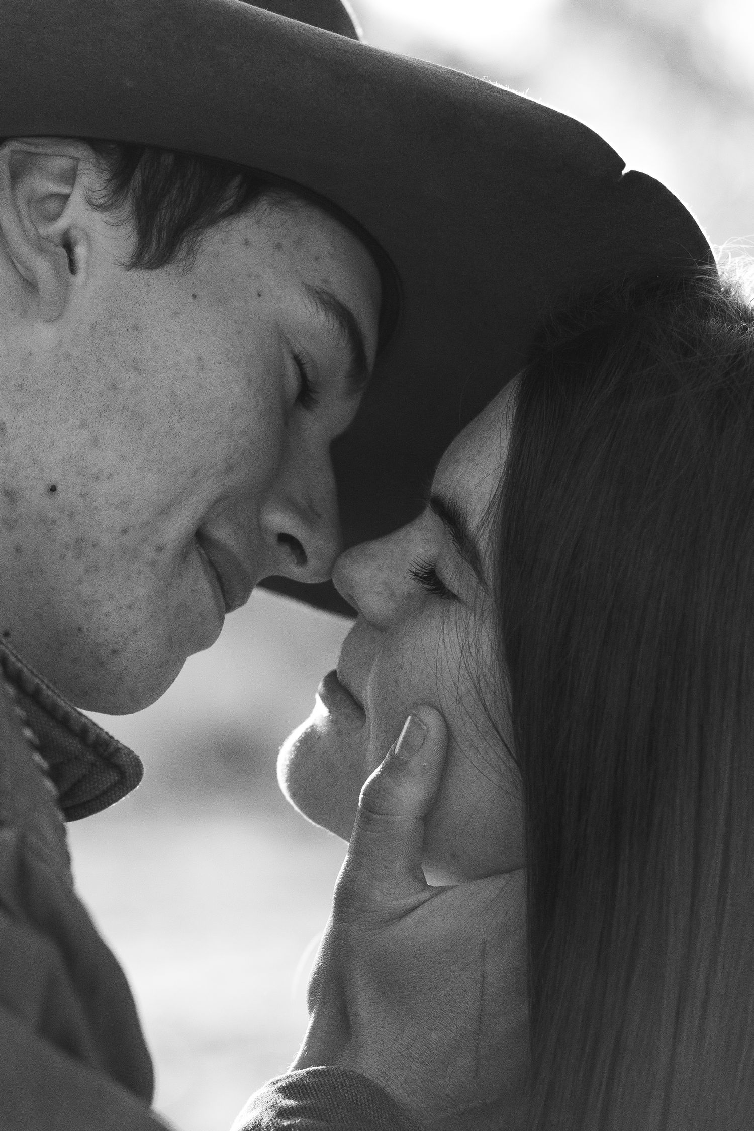 Intimate close-up black and white portrait of couple in western wear sharing tender moment.