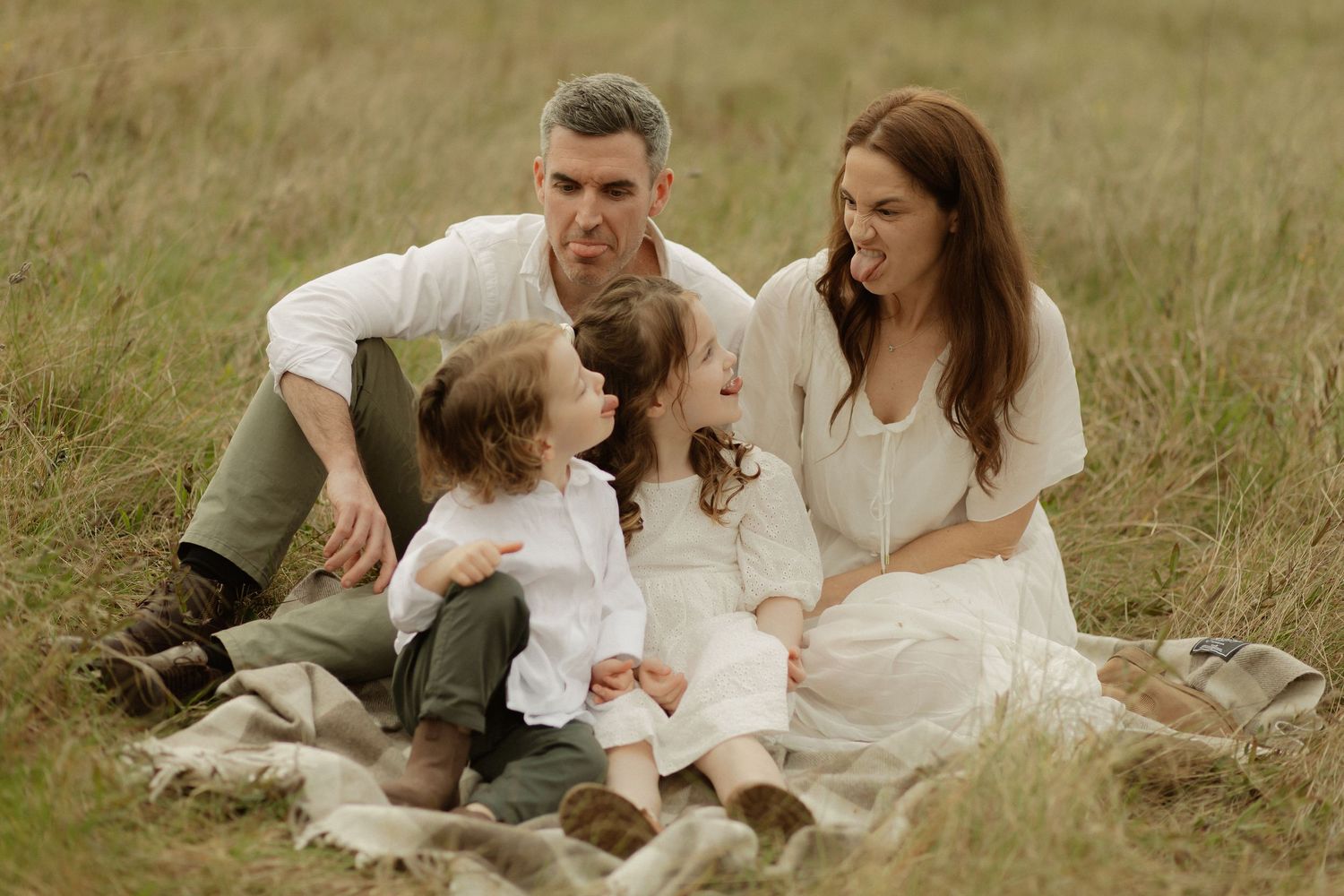A family enjoys a picnic together on a blanket spread out in a grassy meadow.