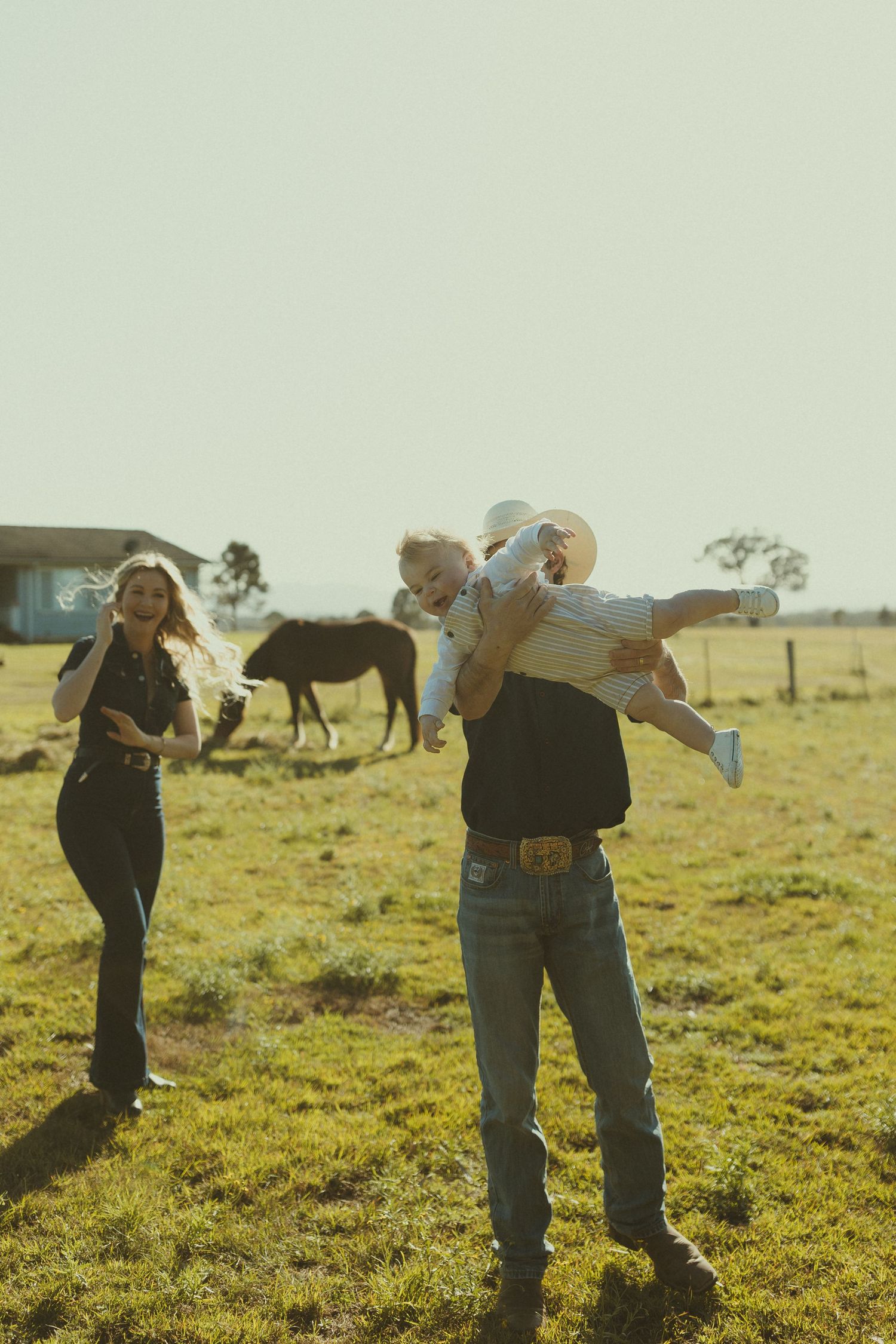 Two people in western attire play together on a grassy field during golden hour.