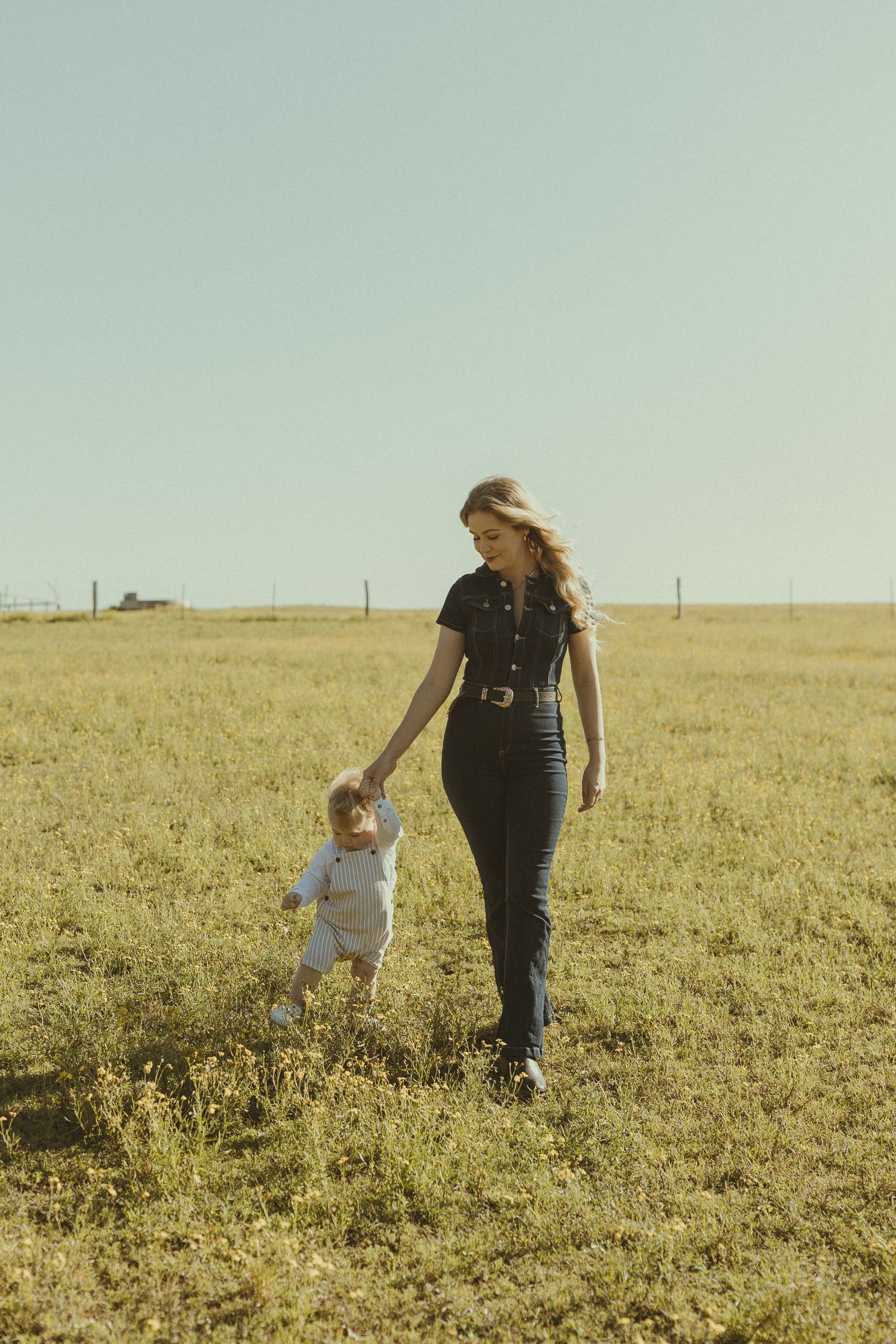 A parent and child walk together through a sunlit meadow on a bright afternoon.