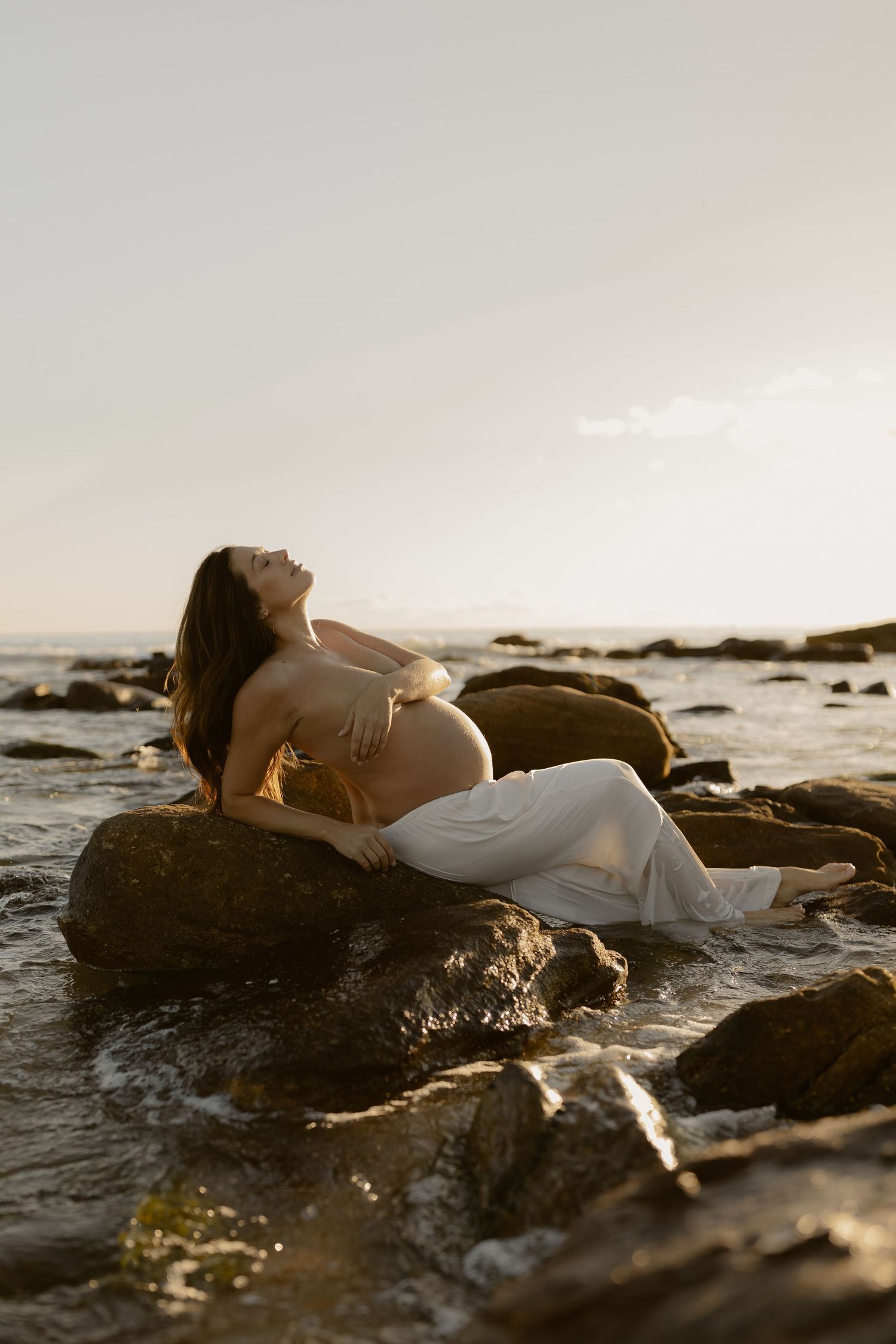 A maternity photo session on rocky coastal shores at golden hour.