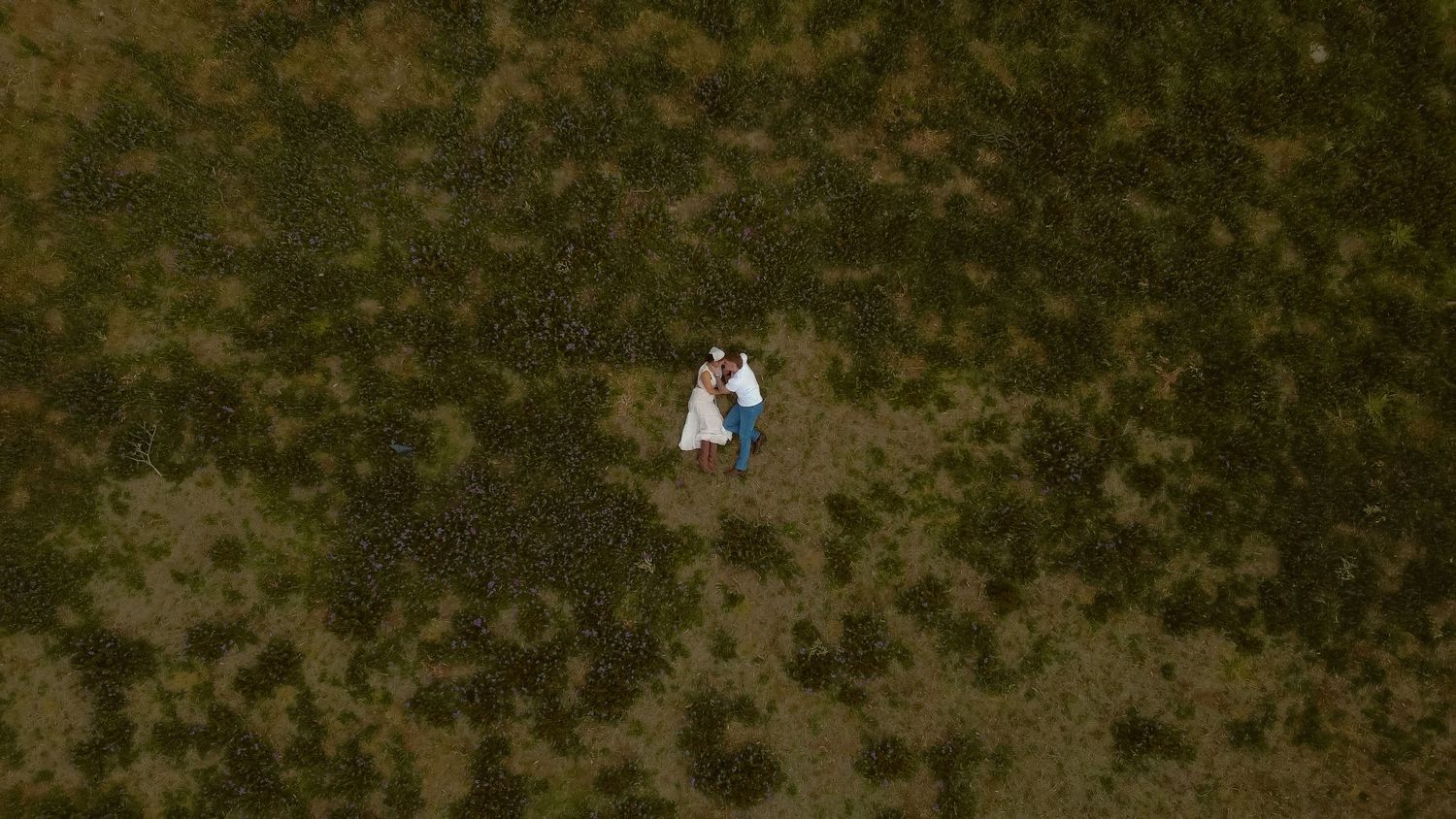 Aerial view of two people in white standing in a vast green field.