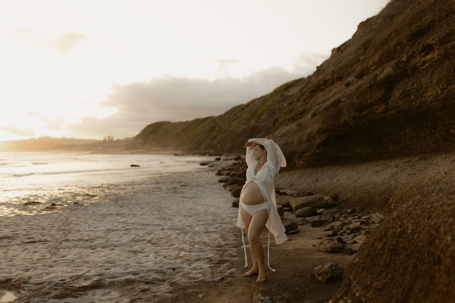 Scenic beach photoshoot at golden hour with rocky cliffs and gentle waves along the shoreline.