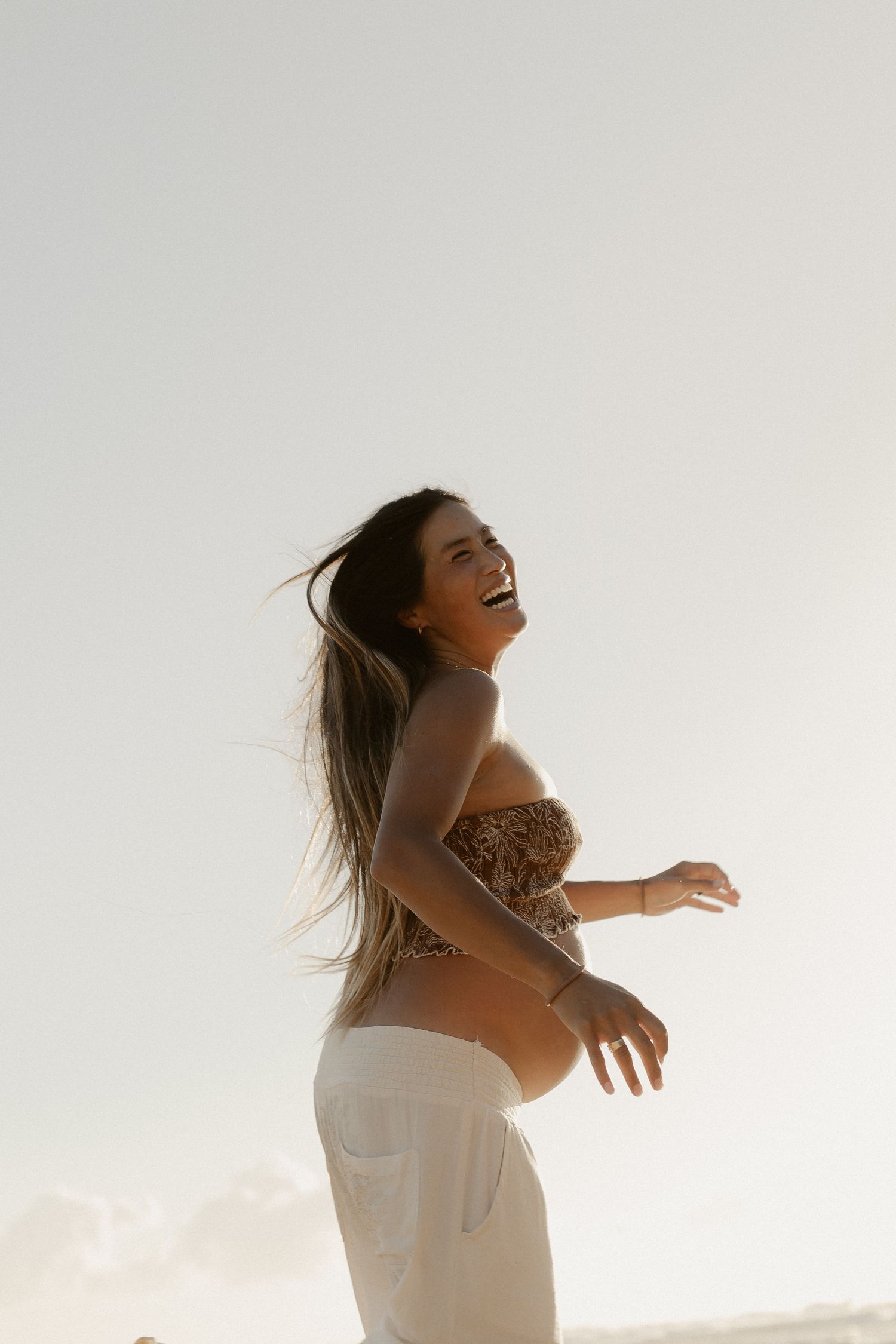 A woman in white clothing dances freely against a bright sky background.