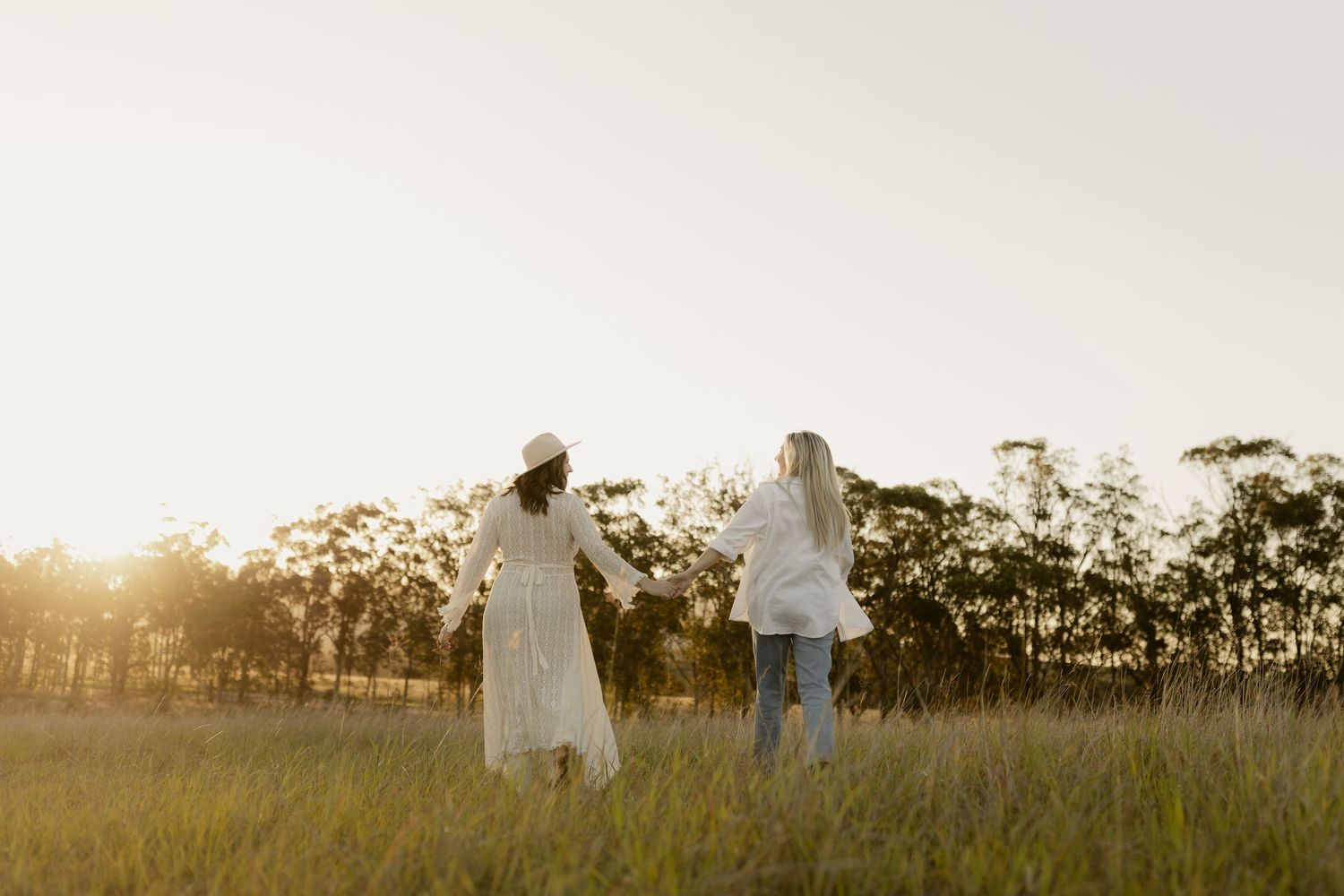 Silhouettes of figures walking through a golden field at sunset with trees in the background.