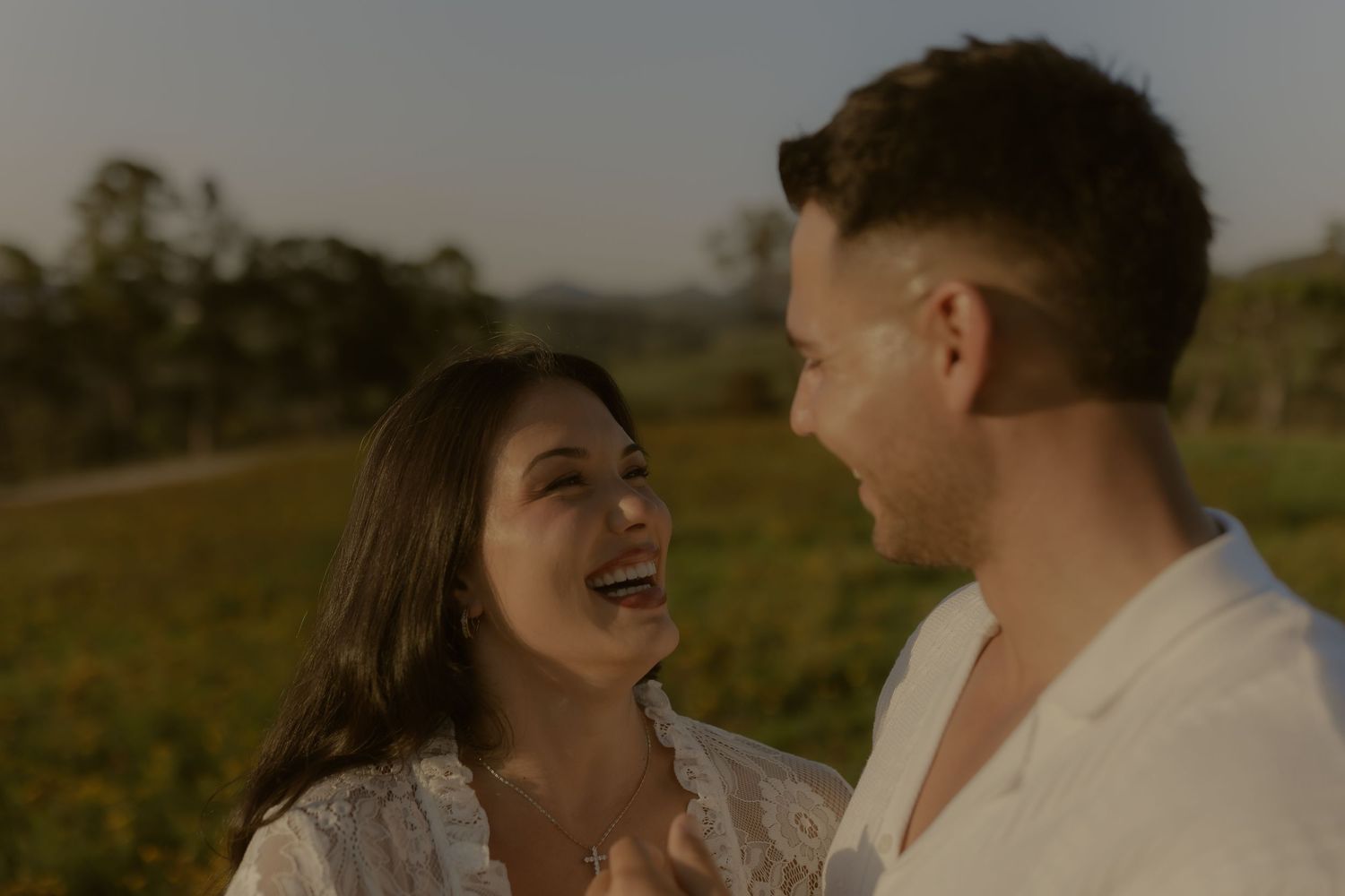 A couple shares a joyful laugh together in an outdoor setting during golden hour.