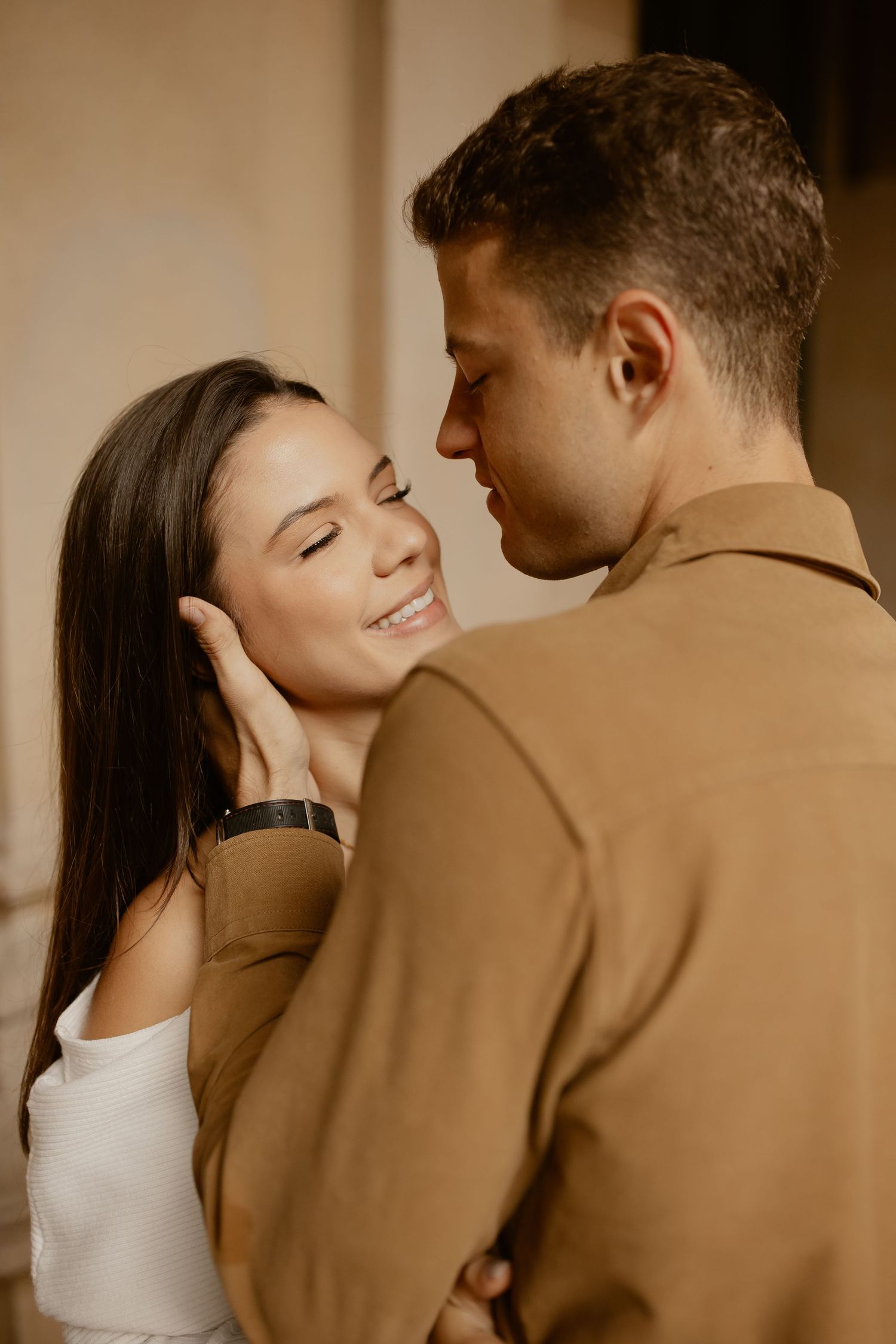 Romantic couple embraces in warm lighting, with one wearing a brown sweater and the other in white.