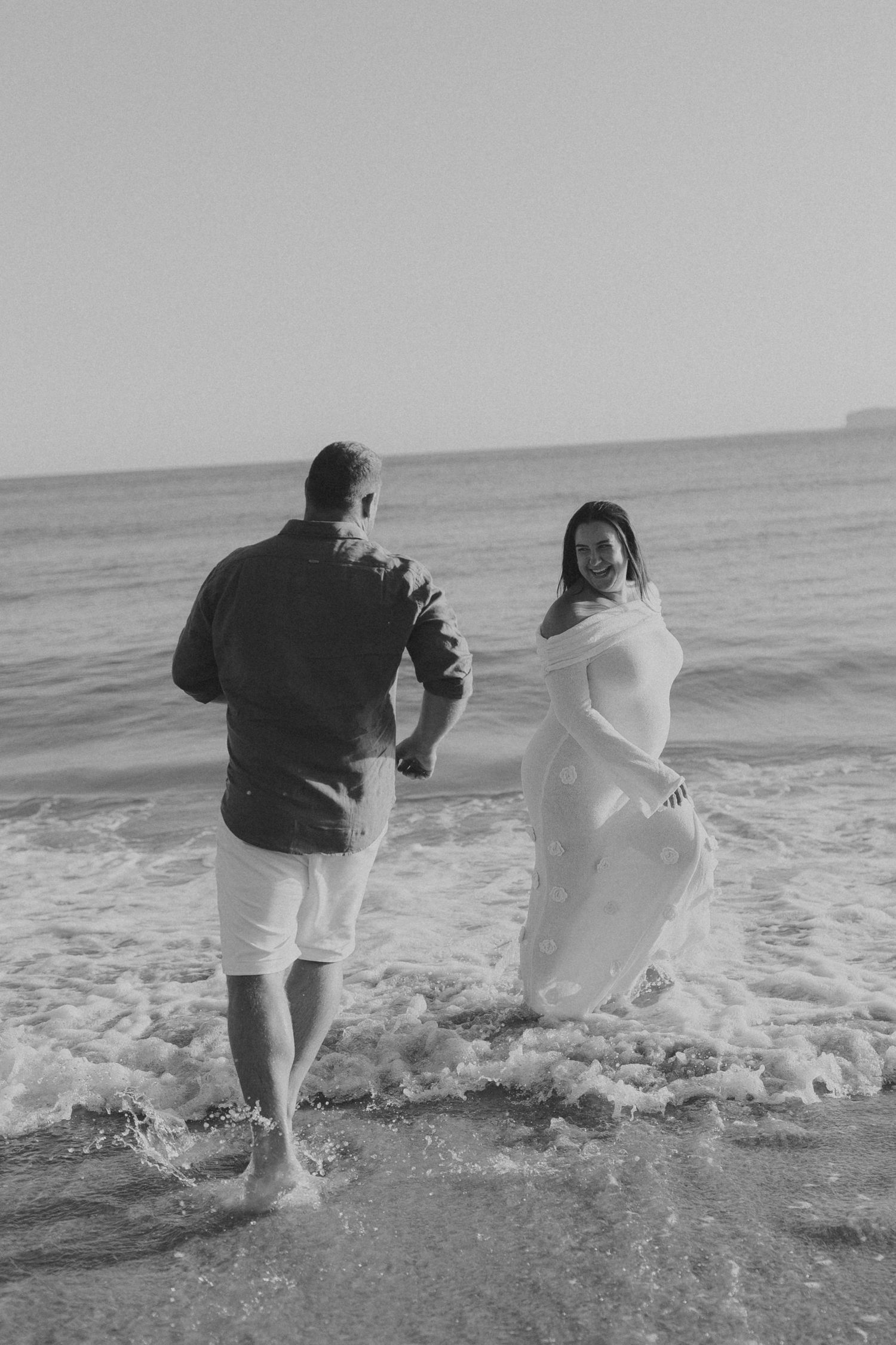 A couple playing in the ocean waves, with the person in white dress getting splashed.