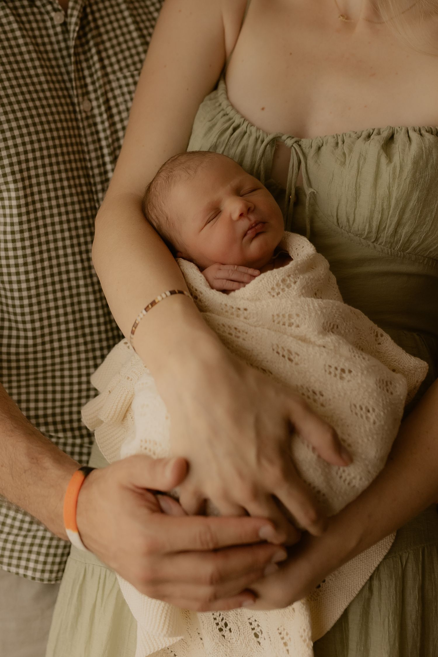 Infant sleeping peacefully in arms against checkered fabric background.