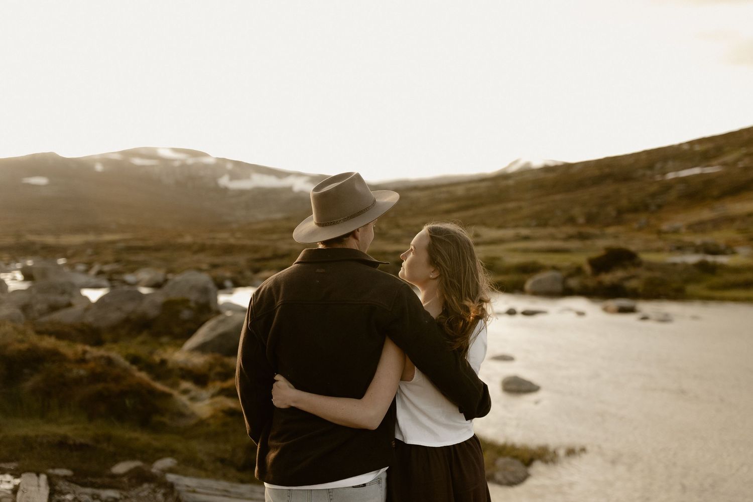 A romantic couple embraces on a scenic beach during sunset in a sepia-toned photograph.