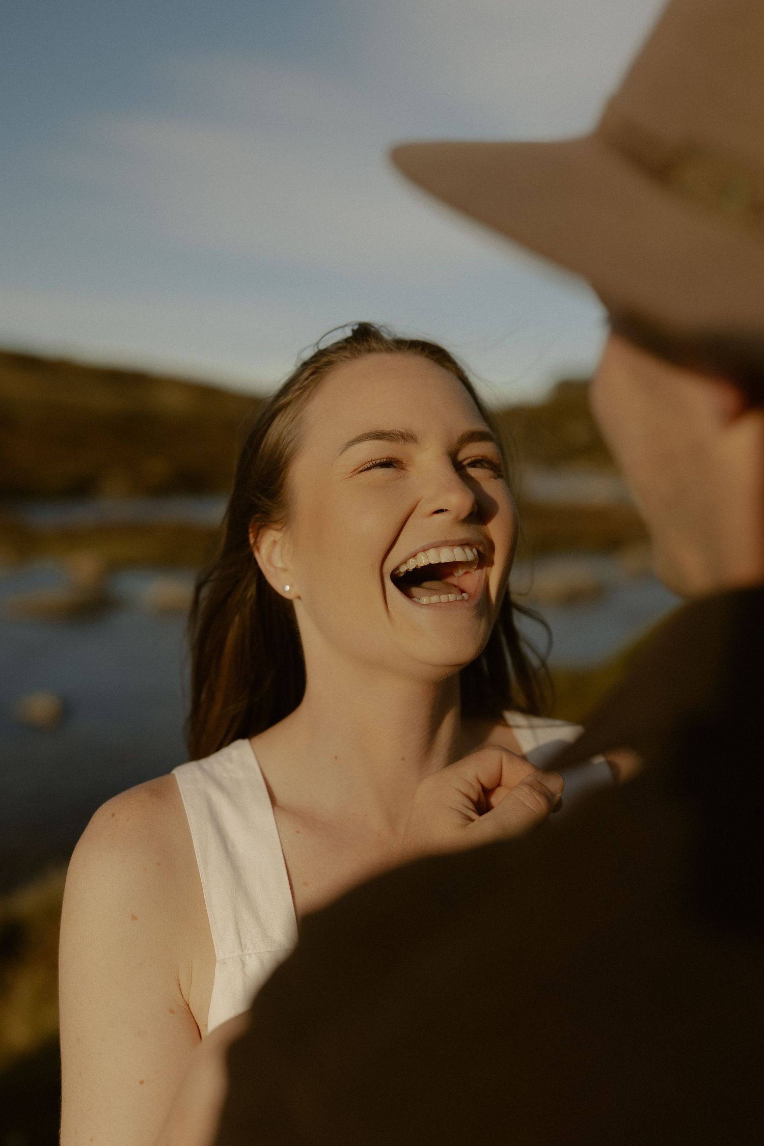 A joyful moment captured between two people laughing together outdoors by the water.