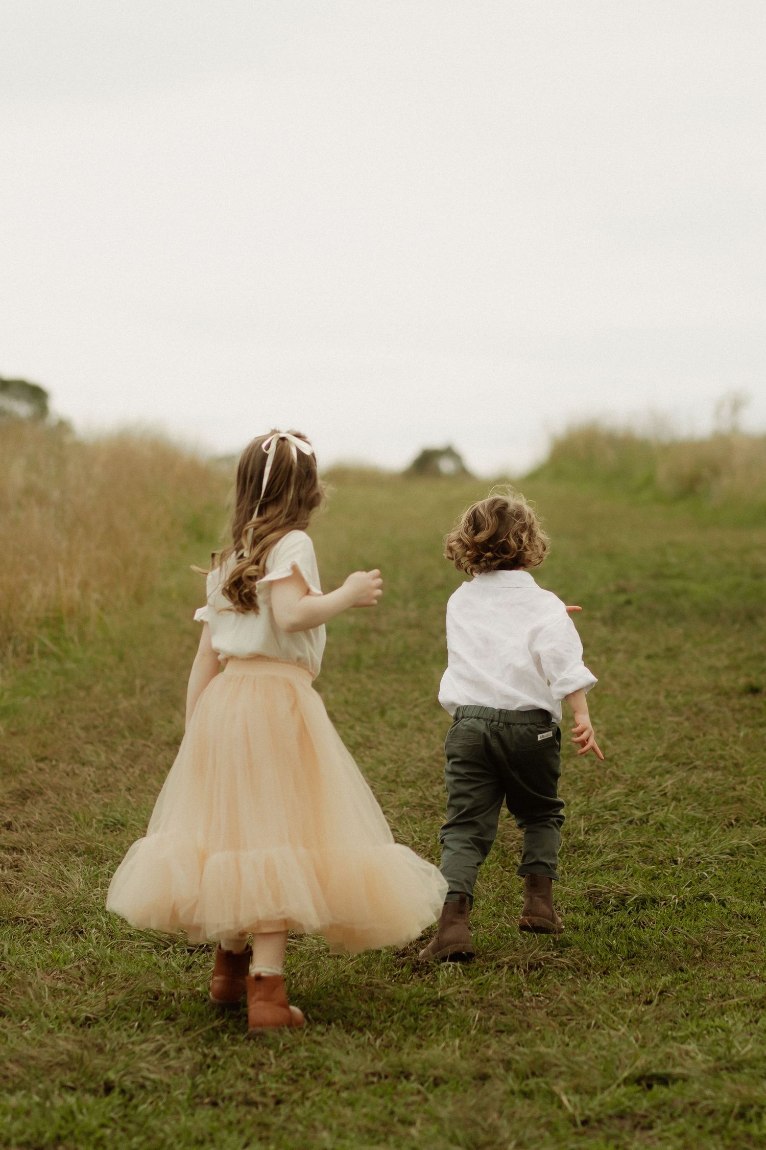 Children running and playing together in a grassy field wearing formal attire.
