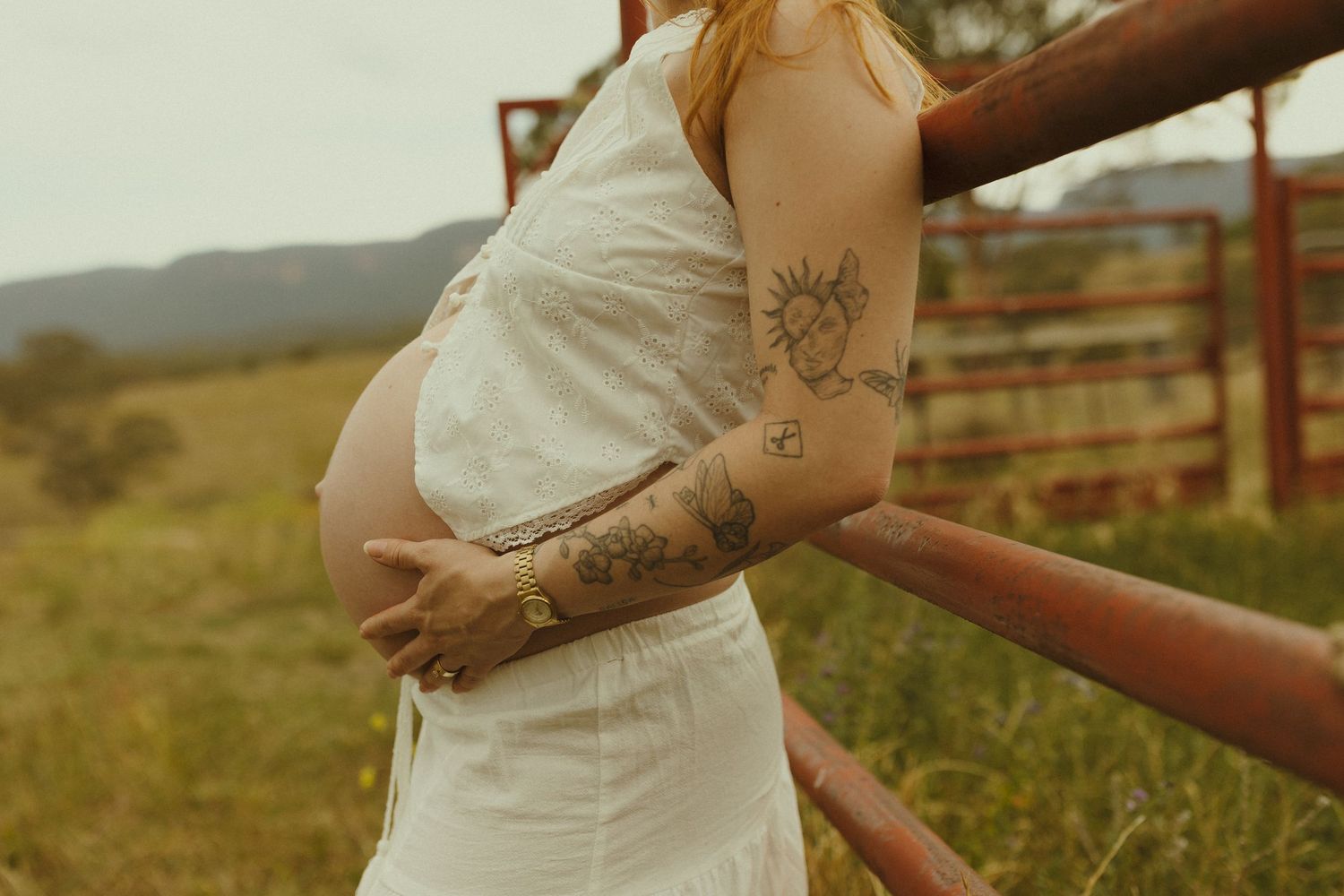 Close-up details of a white lace wedding dress against rustic wooden fence posts in natural lighting.