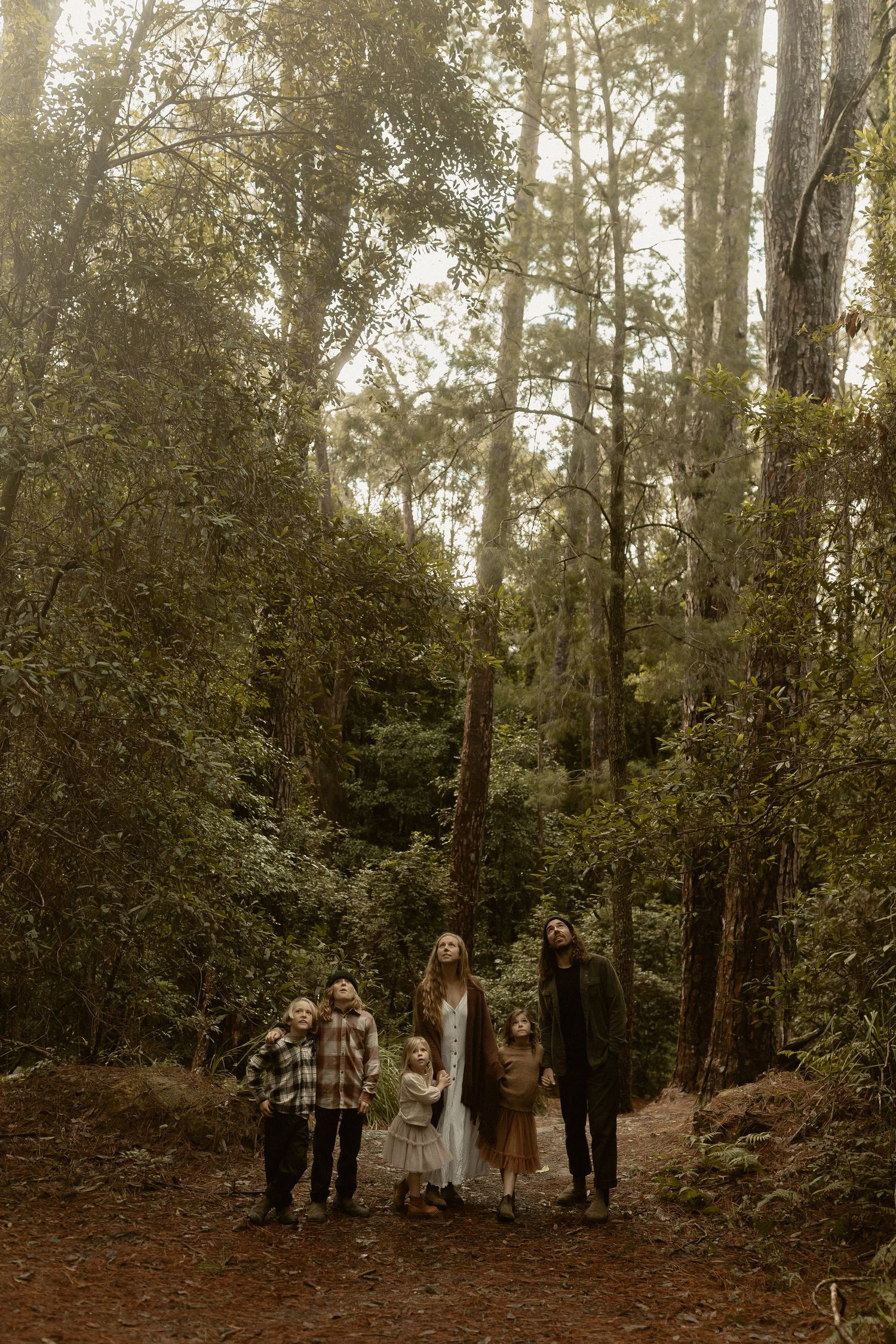 A group in vintage clothing stands together in a misty forest setting with tall trees in the background.