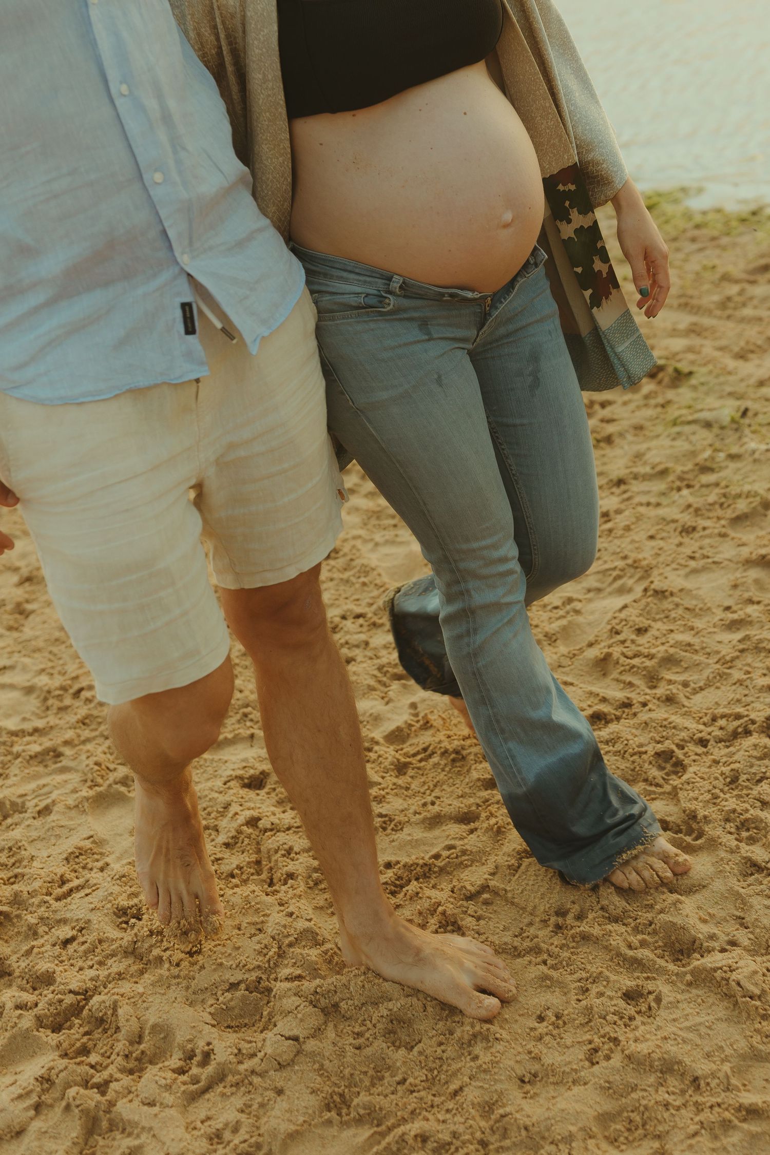 Bare feet stand in soft sand during a beach photoshoot at golden hour.