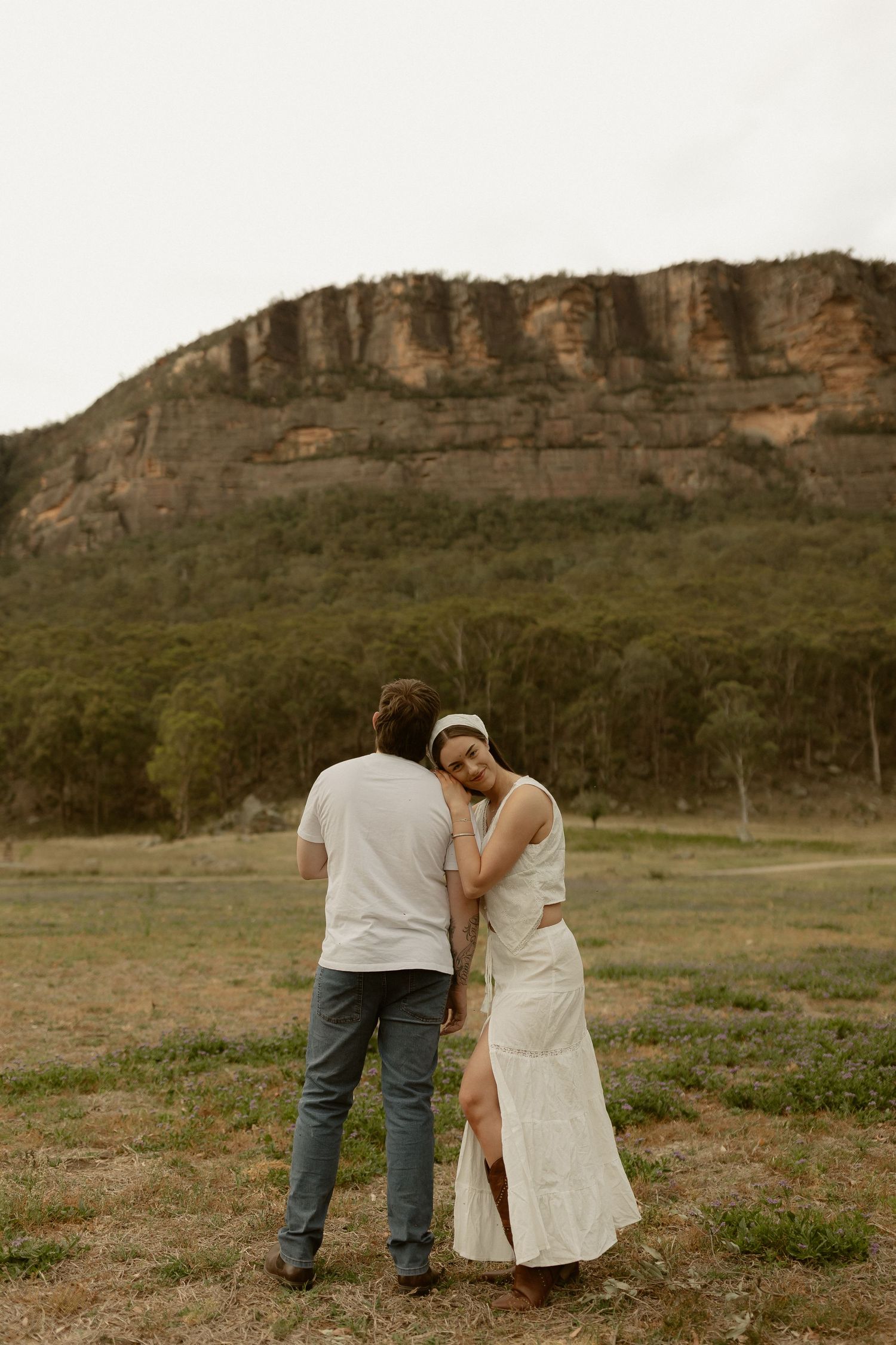 Two people sharing an intimate moment against a dramatic cliff backdrop in a rustic outdoor setting.