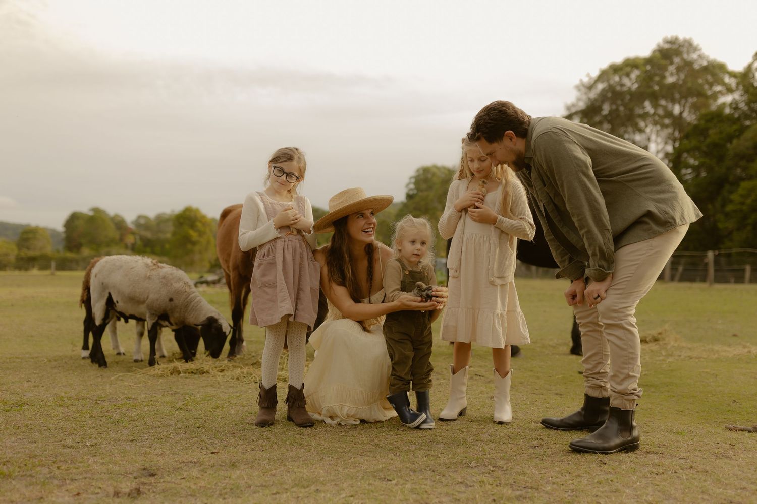 A family with children interacts with farm animals including sheep and a pony in a field.