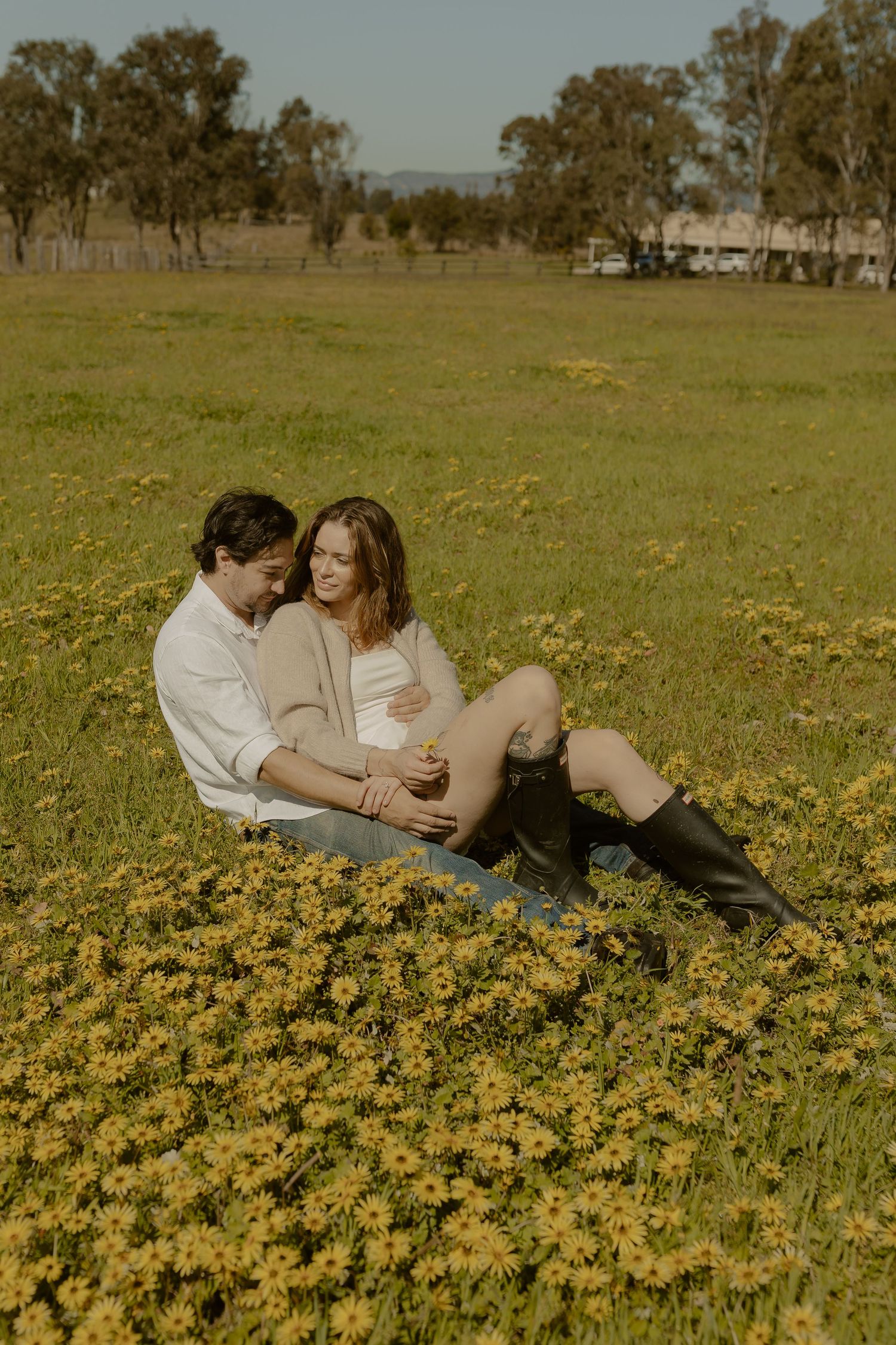 A couple shares an intimate moment while laying in a field of vibrant yellow wildflowers on a sunny afternoon.
