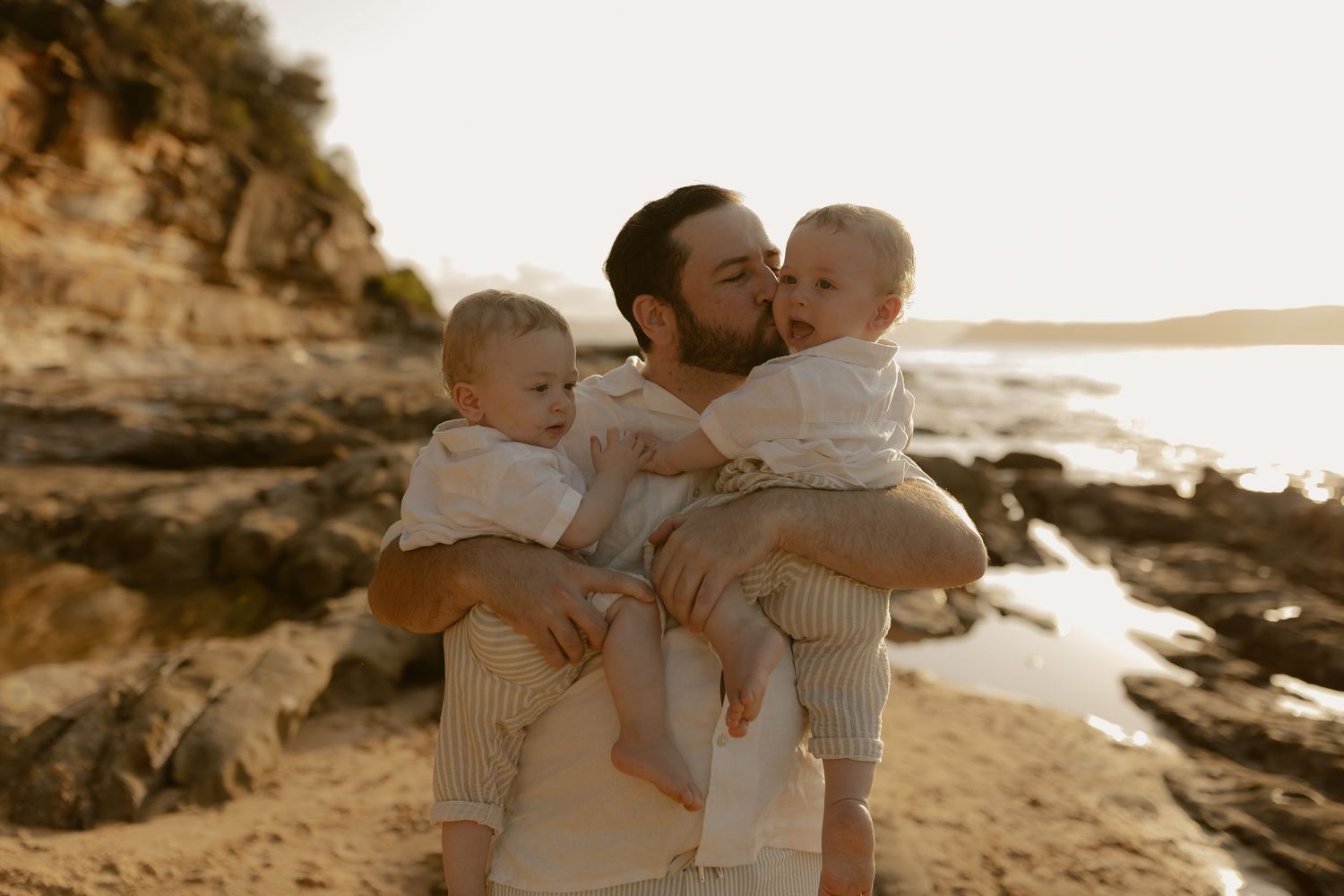 Family embracing on rocky coastline during sunset photoshoot.