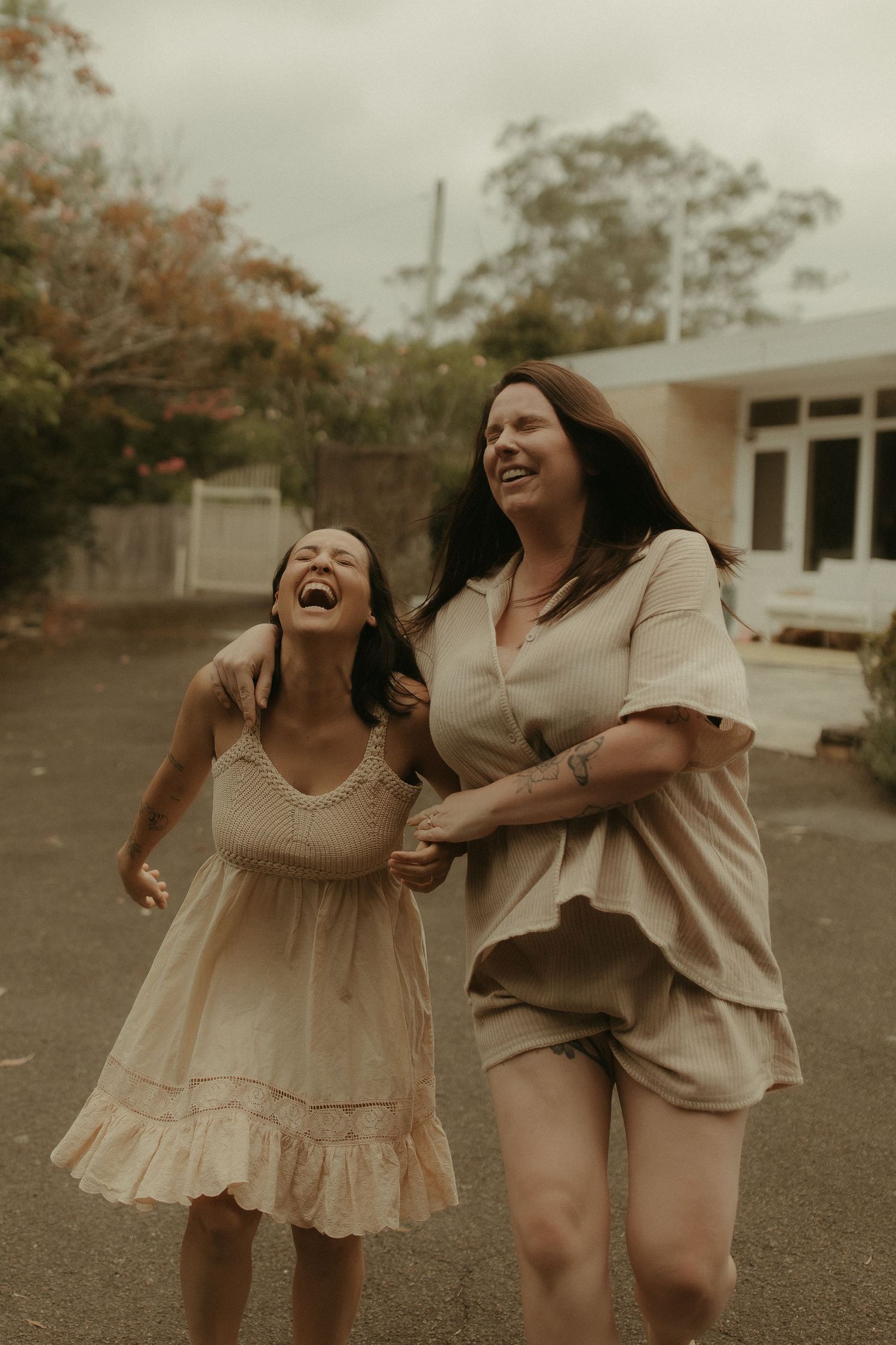 Two people in light colored outfits share a joyful moment laughing together outdoors.