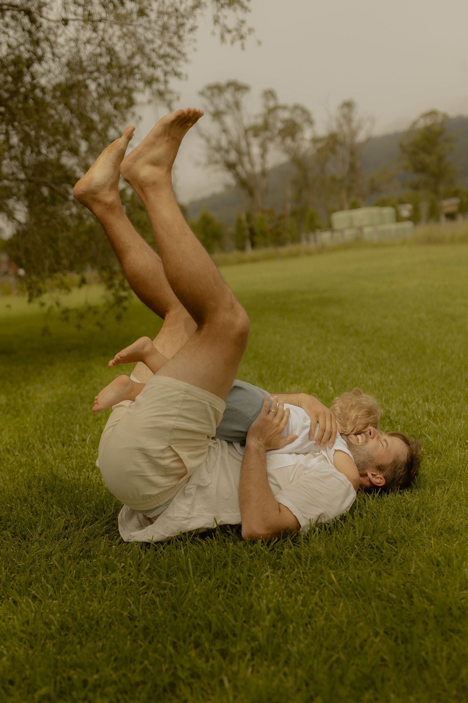 Playful moment lying in grass with legs up against a rural backdrop.