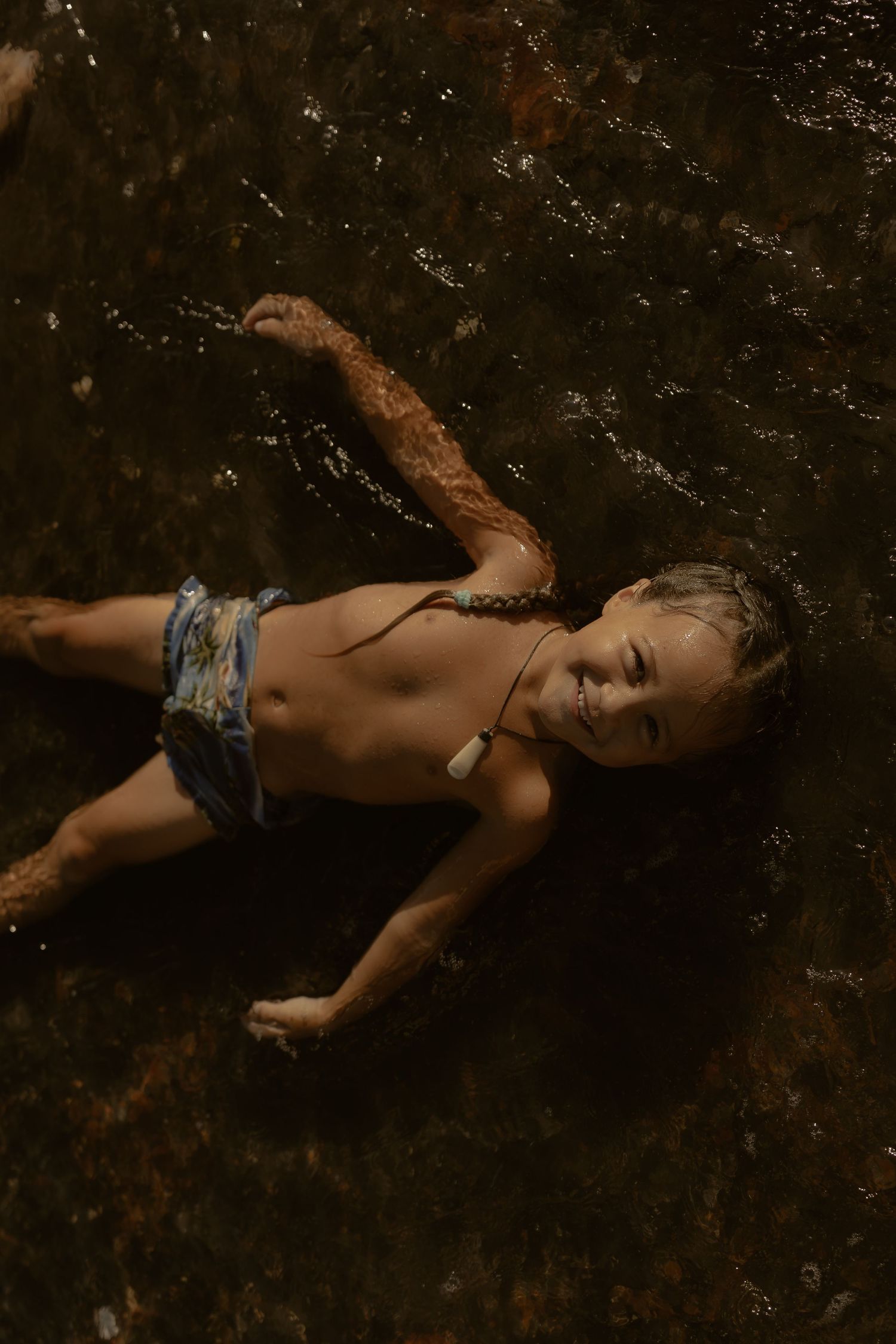 Child floating peacefully in dark water wearing blue patterned swimwear.