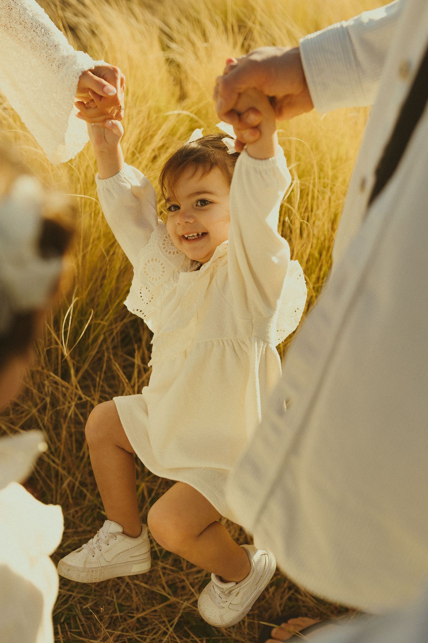 A child wearing a white dress plays joyfully in a golden wheat field during sunset.