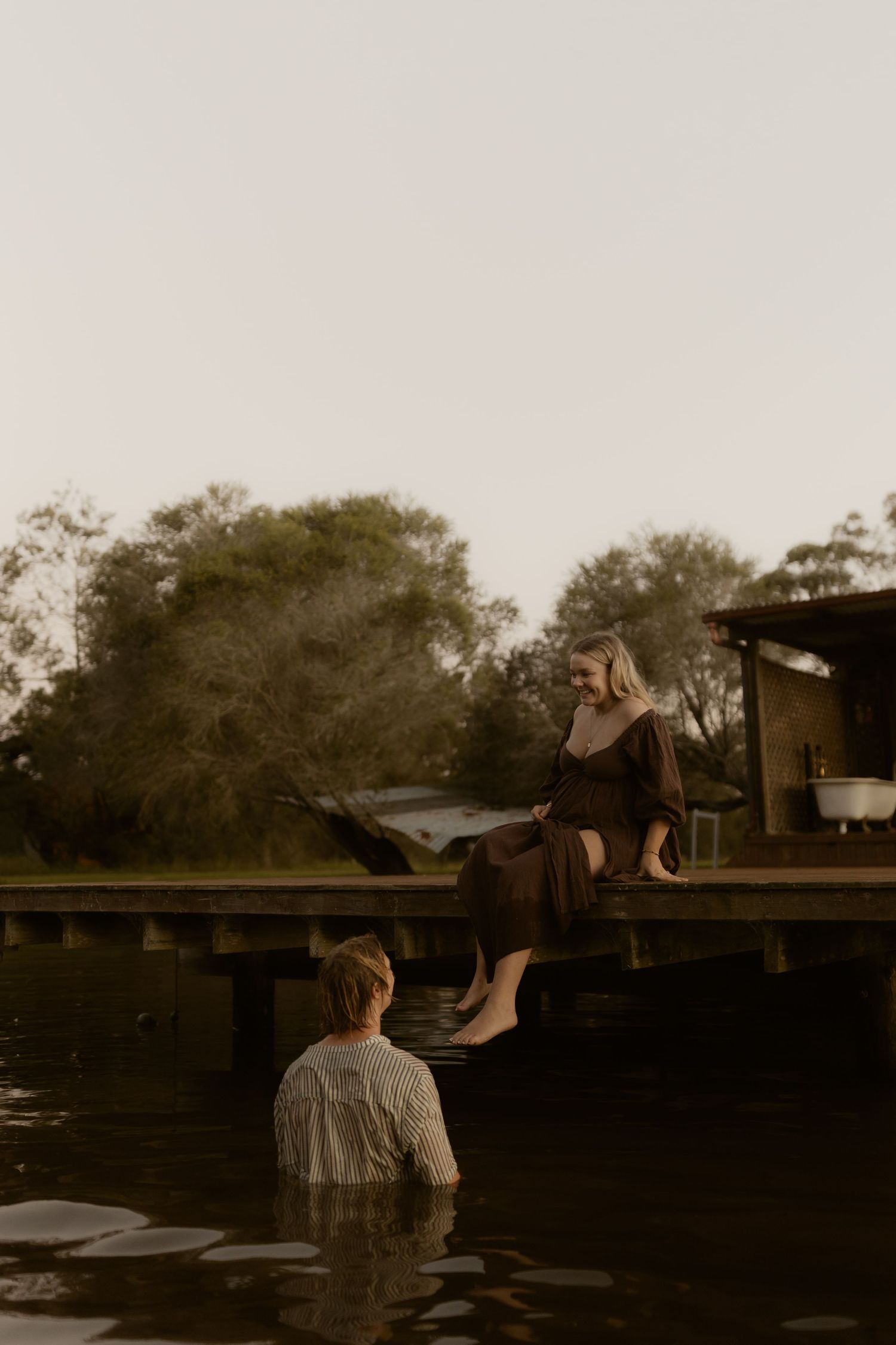 Sunset silhouettes of people sitting on a dock by a tranquil lake.