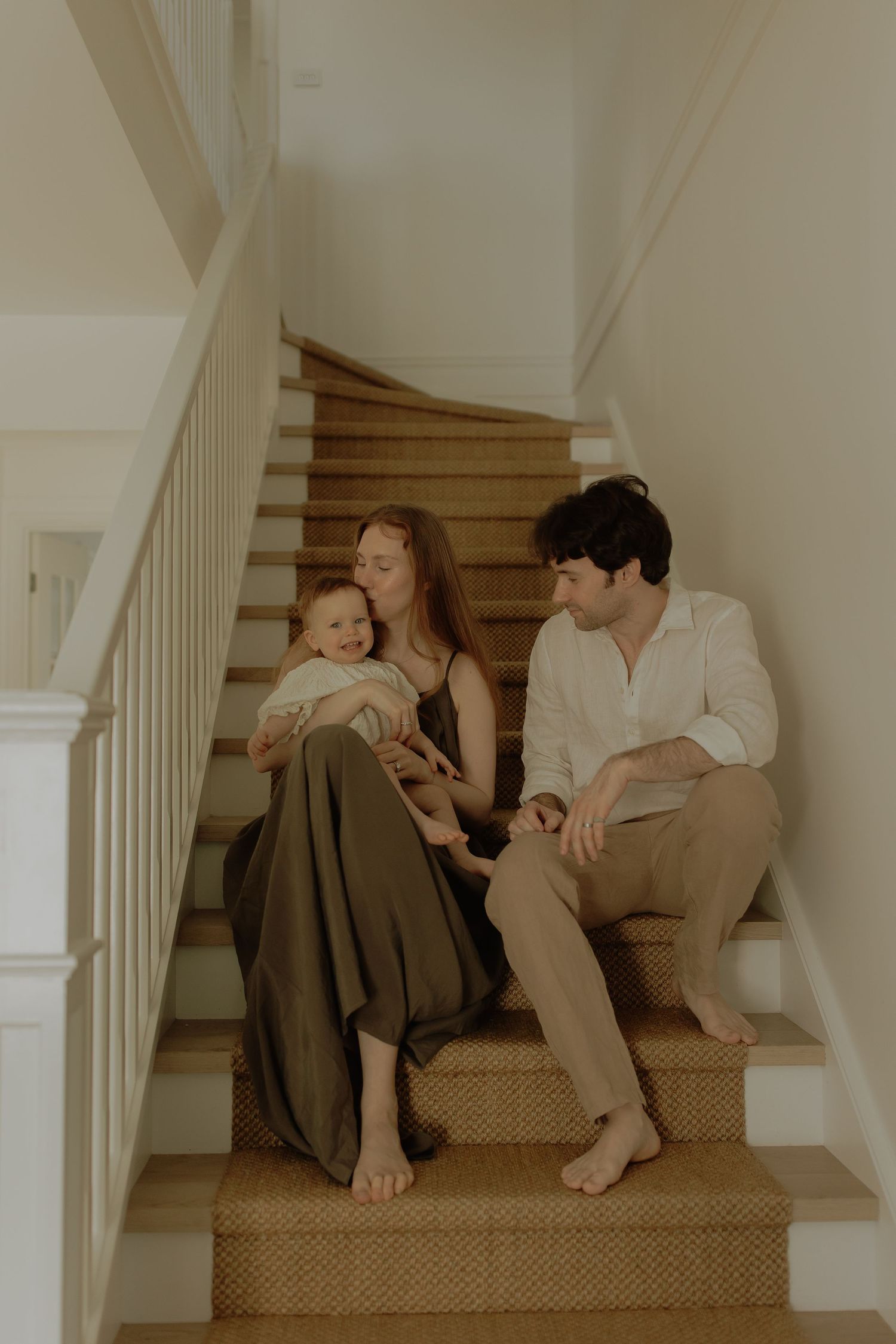 A young family with a baby sits together on wooden staircase steps at home.