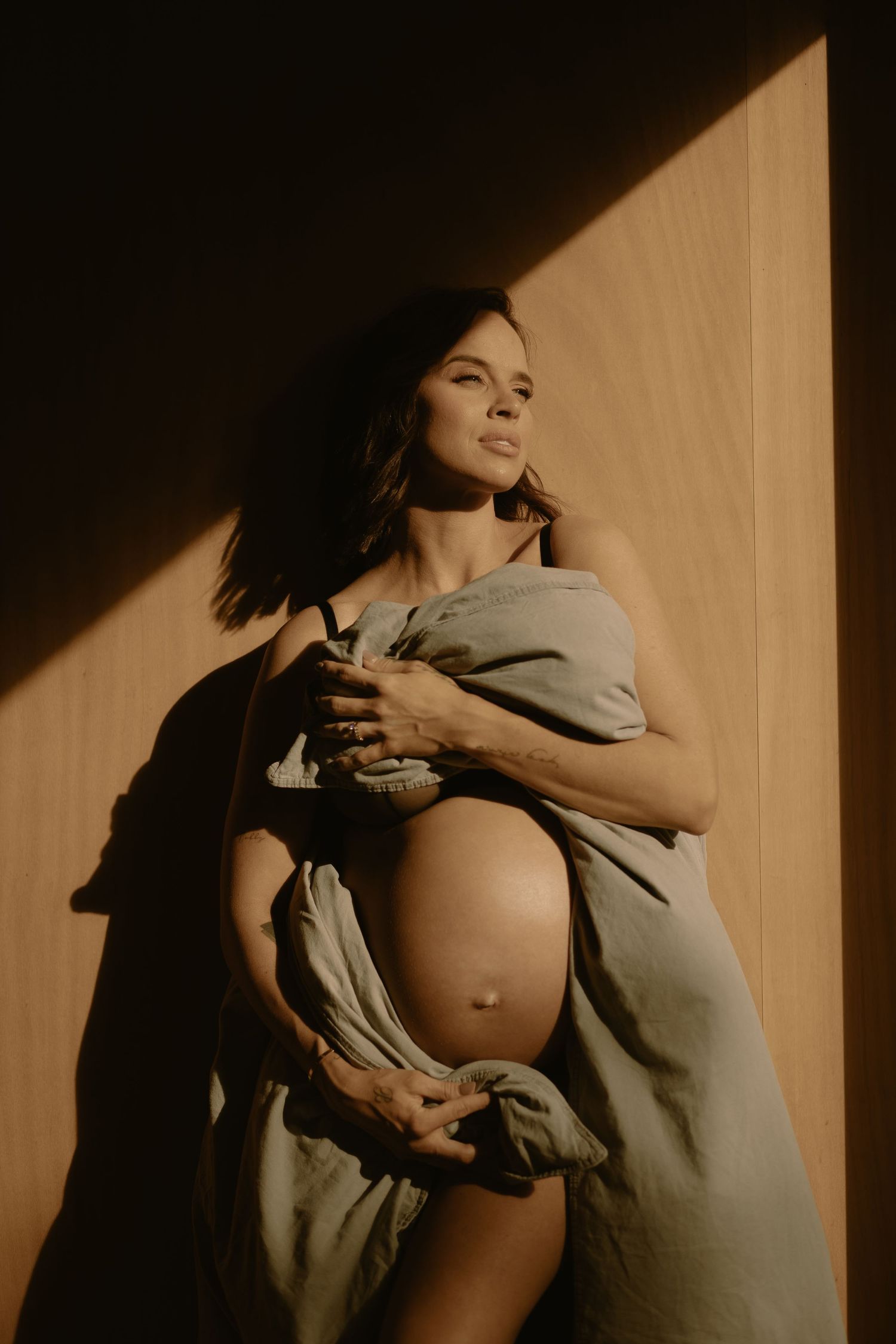 A dramatic maternity portrait with strong shadows and soft fabric draping around the pregnant belly.