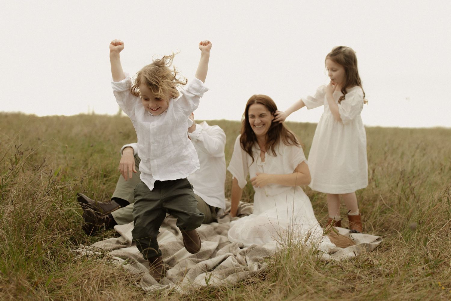 A romantic wedding couple and guests celebrate in a rustic outdoor field setting during golden hour.