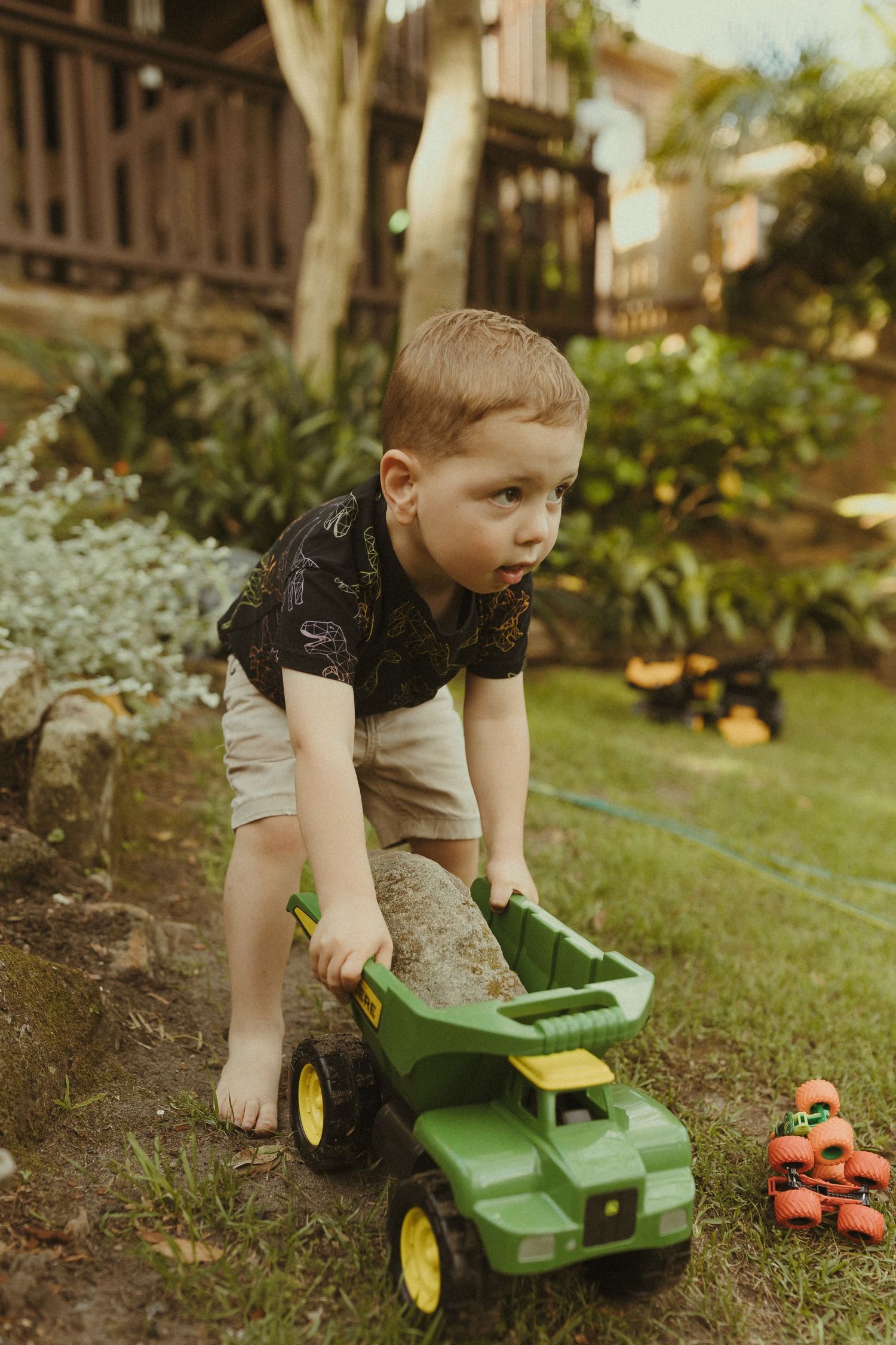 A child playing with a green toy tractor in a garden.