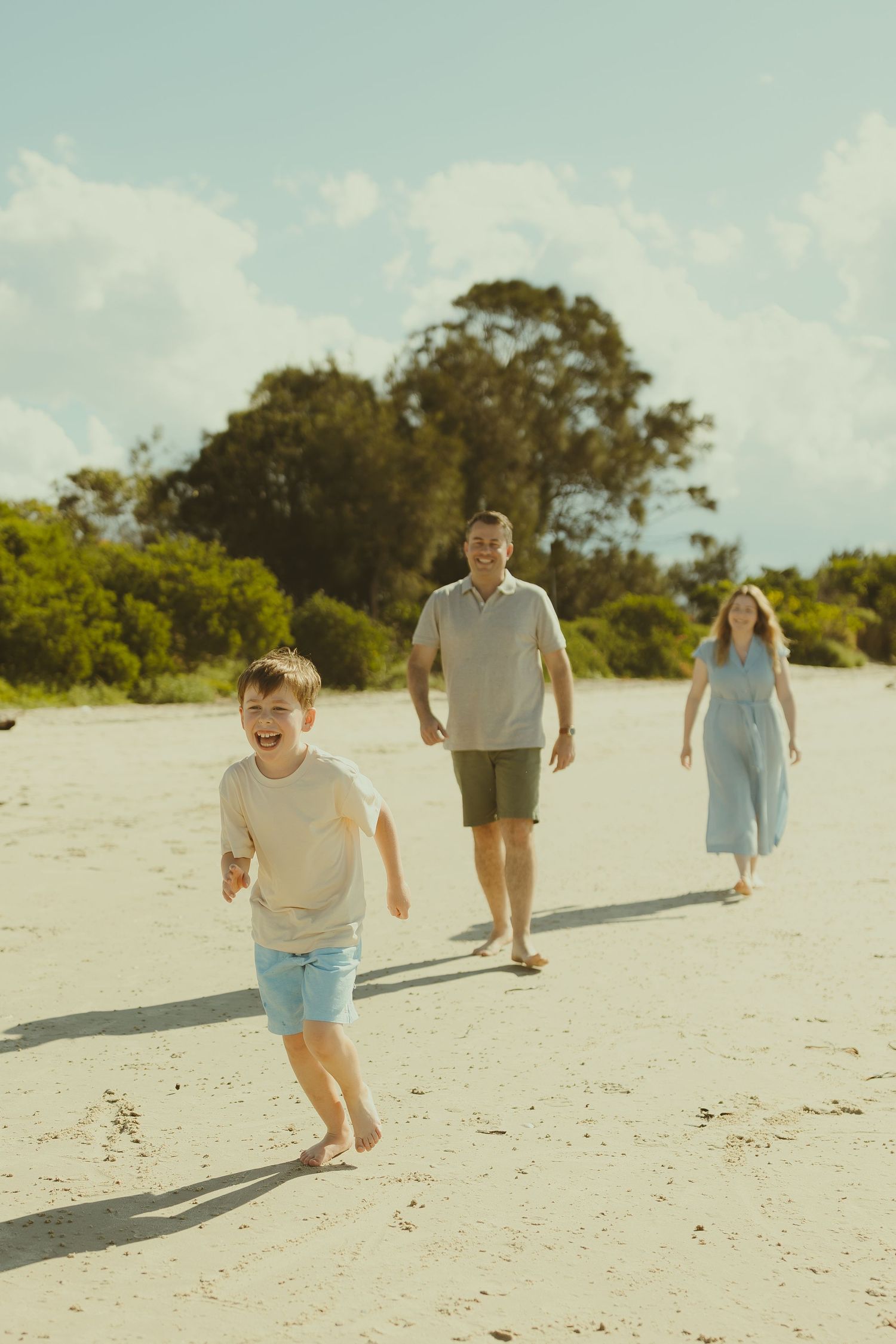 People enjoying a playful moment running on a bright tropical beach with trees in the background.