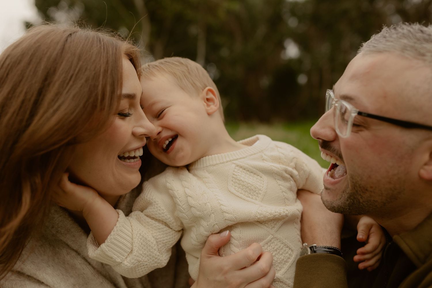 Laughing family moment with parents and giggling toddler in outdoor setting.