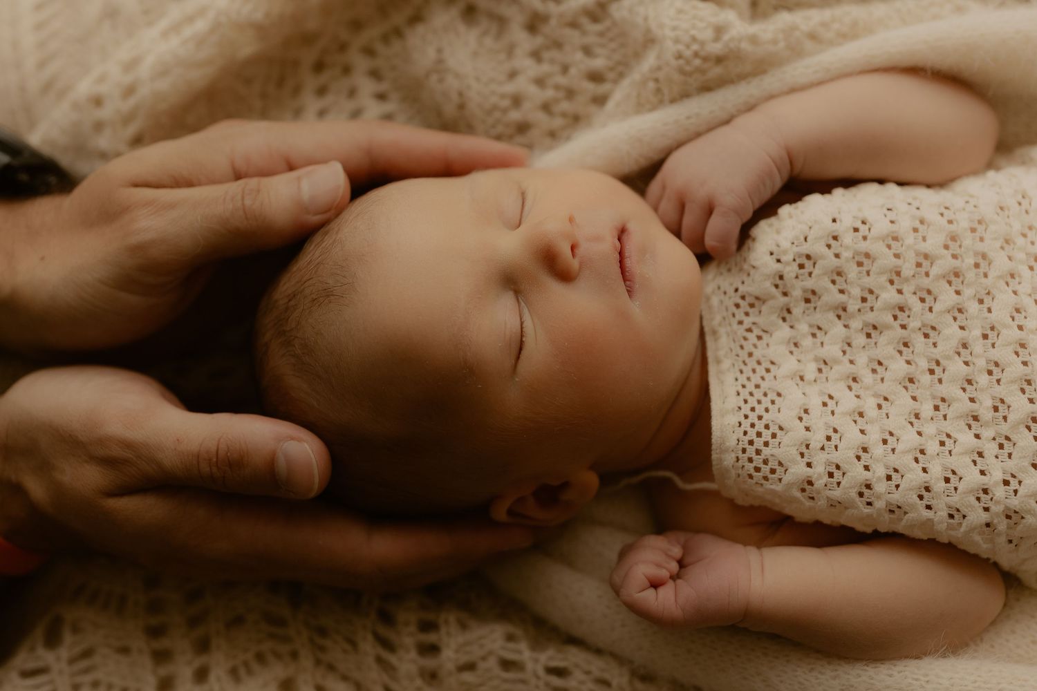 Sleeping baby swaddled in a knit blanket lies peacefully on soft bedding in warm neutral tones.
