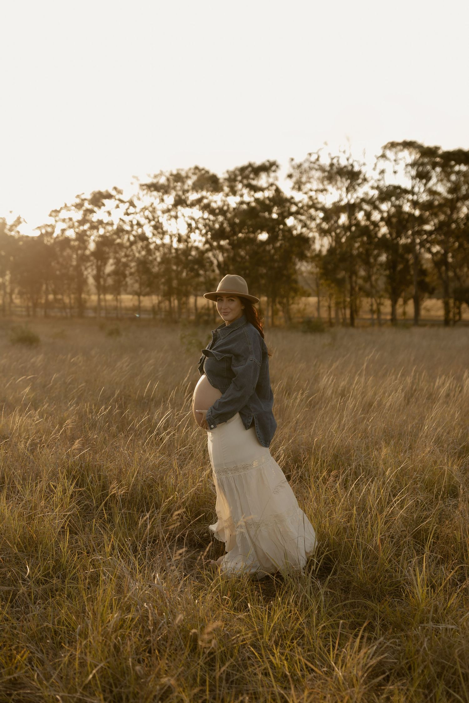 Couple embraces in golden sunlit meadow at sunset with tall grass swaying in the breeze.