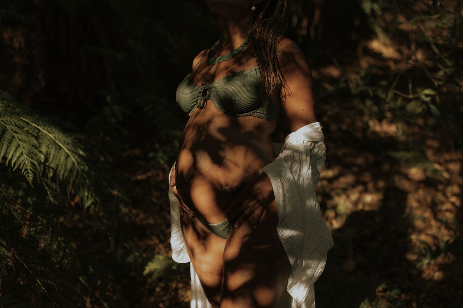 Couple embraces in romantic forest setting with dappled sunlight filtering through trees.