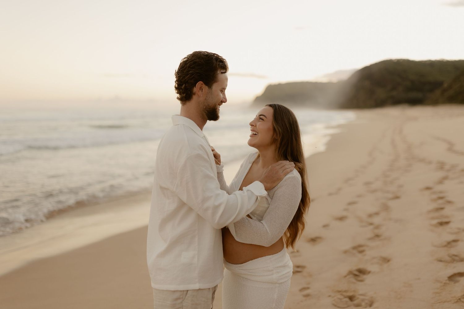 Romantic couple walking together on a sandy beach at sunset with ocean waves in the background.