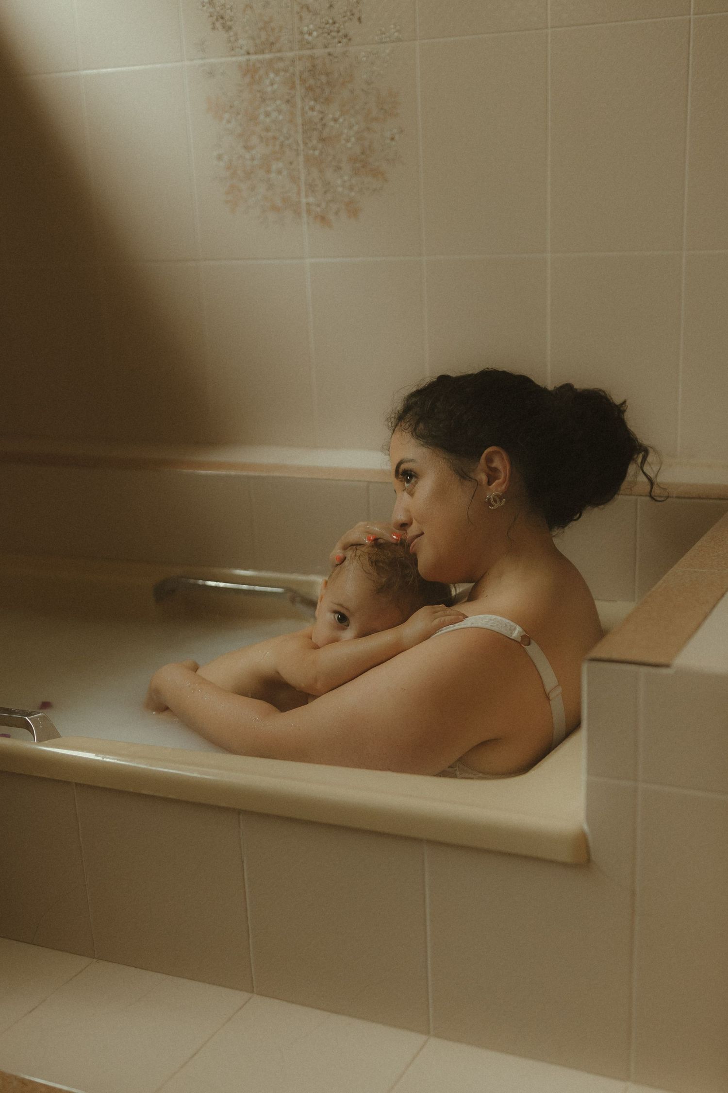 A tender bathtub moment shows a parent and child resting together in soft, warm lighting.