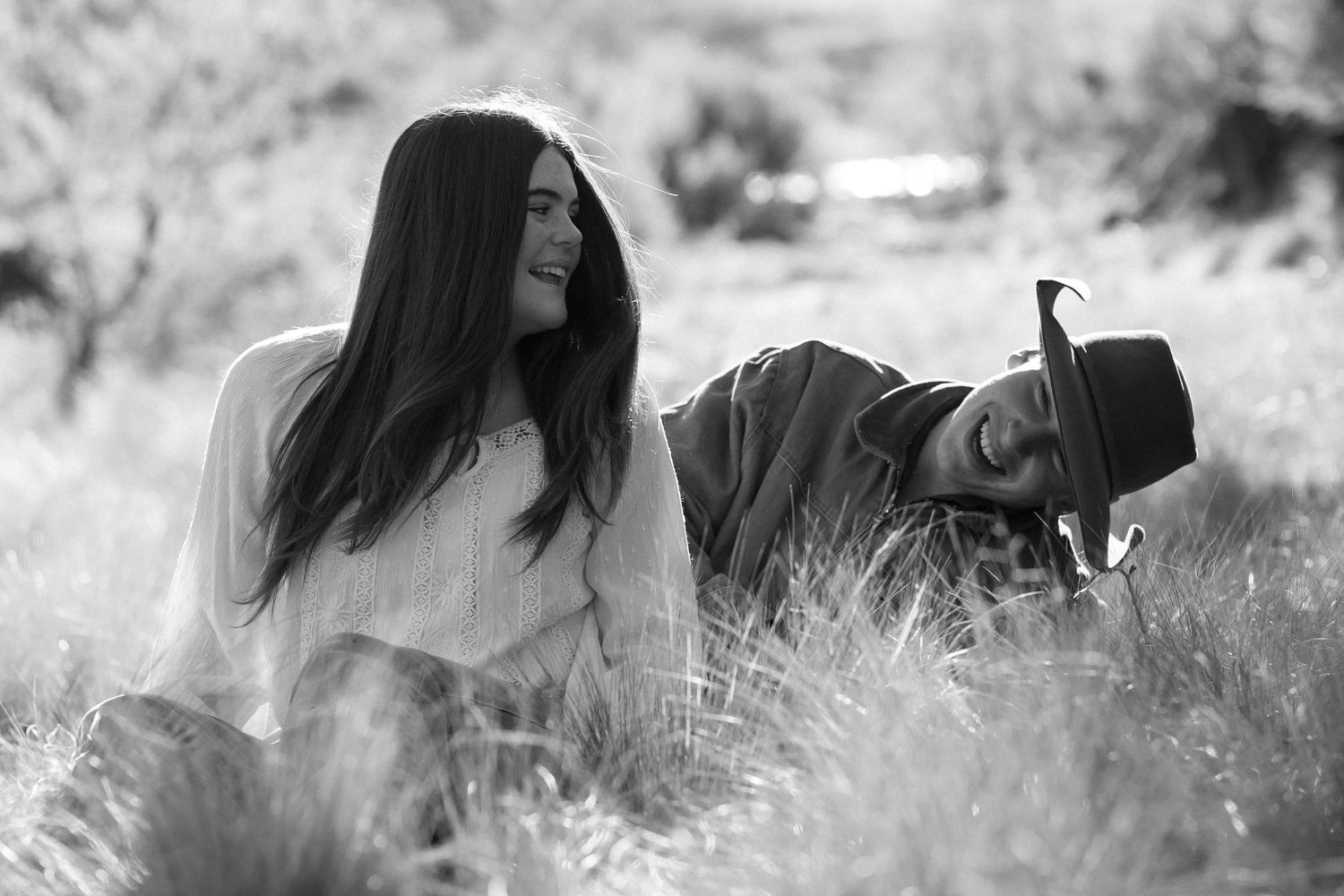 Black and white portrait of person laying in tall grass with long dark hair while looking to the side.