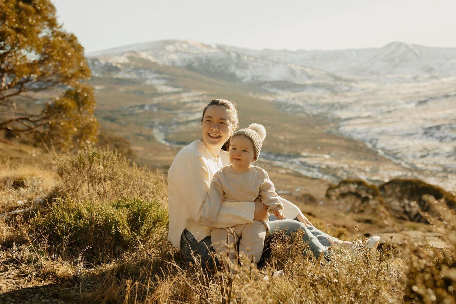 Loving family sitting together on grassy hillside overlooking scenic mountain valley at sunset.