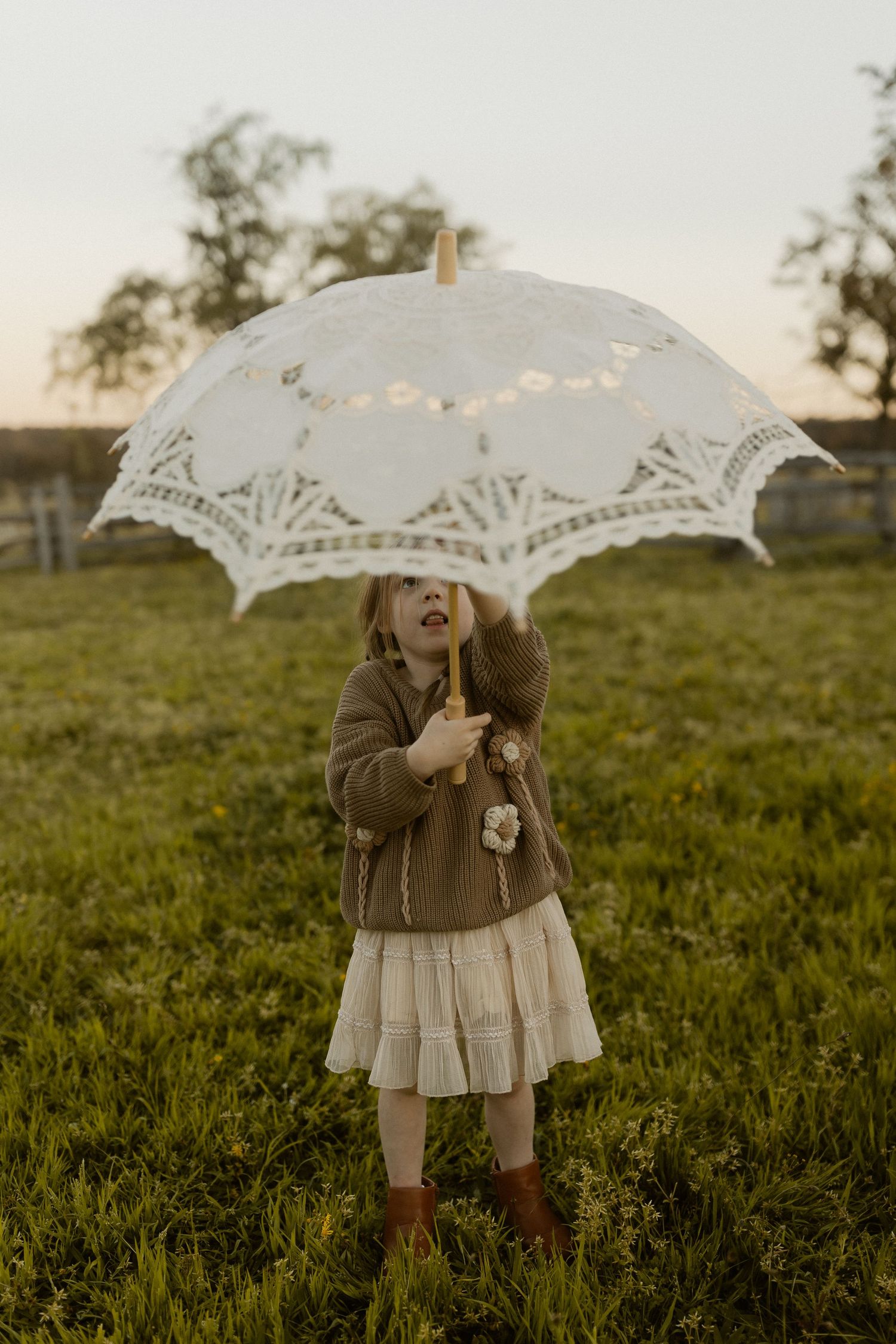 A person holding a delicate lace parasol twirls playfully in a sunlit meadow during golden hour.