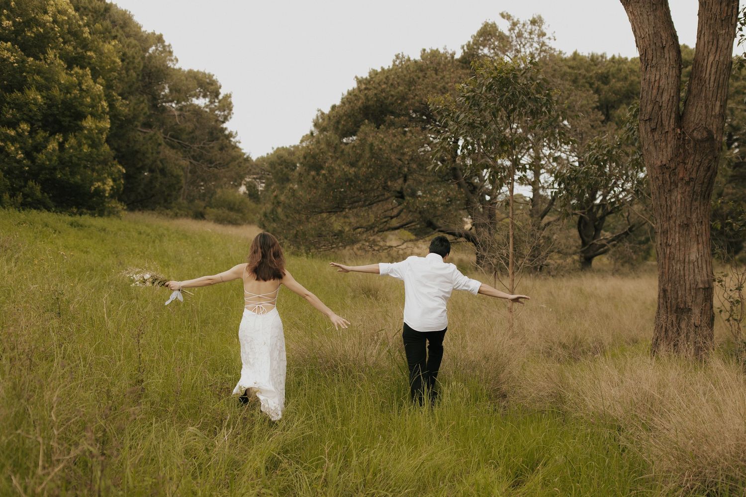 A romantic outdoor photo series showing a couple dancing together in a grassy meadow with trees.