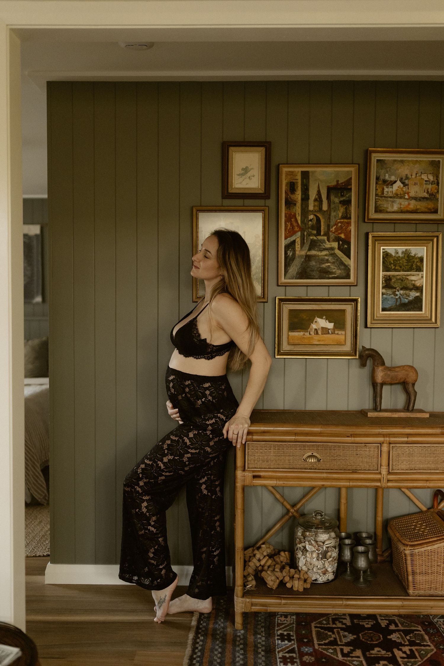 Moody lifestyle photo showing person in black crop top and patterned pants posing against wall with vintage framed artwork.